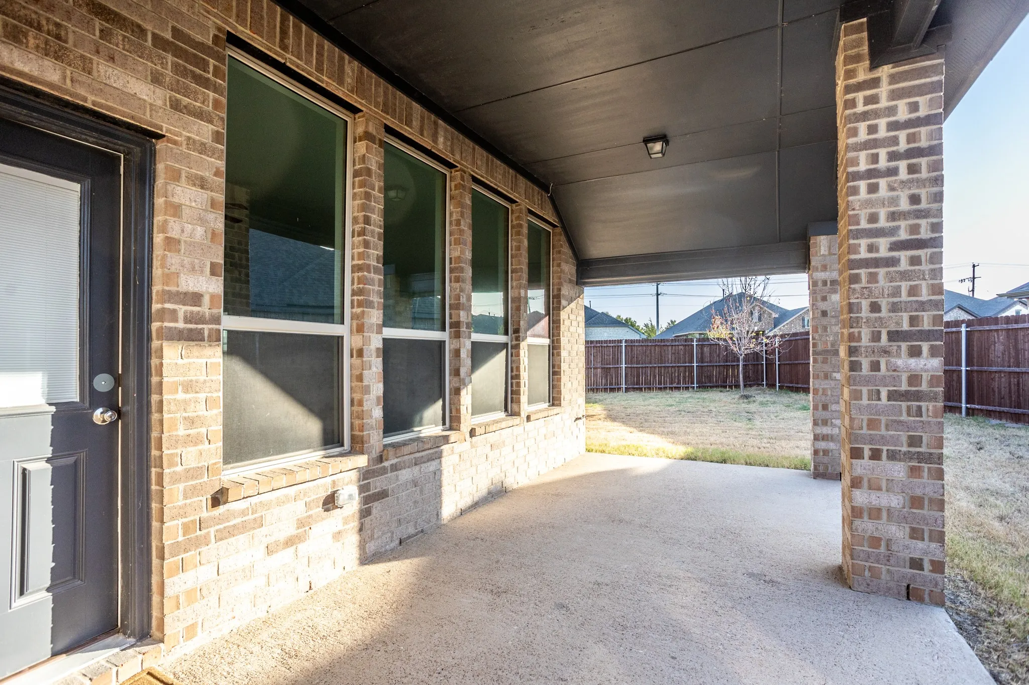 Brick exterior with multiple windows and a covered patio featuring a concrete surface