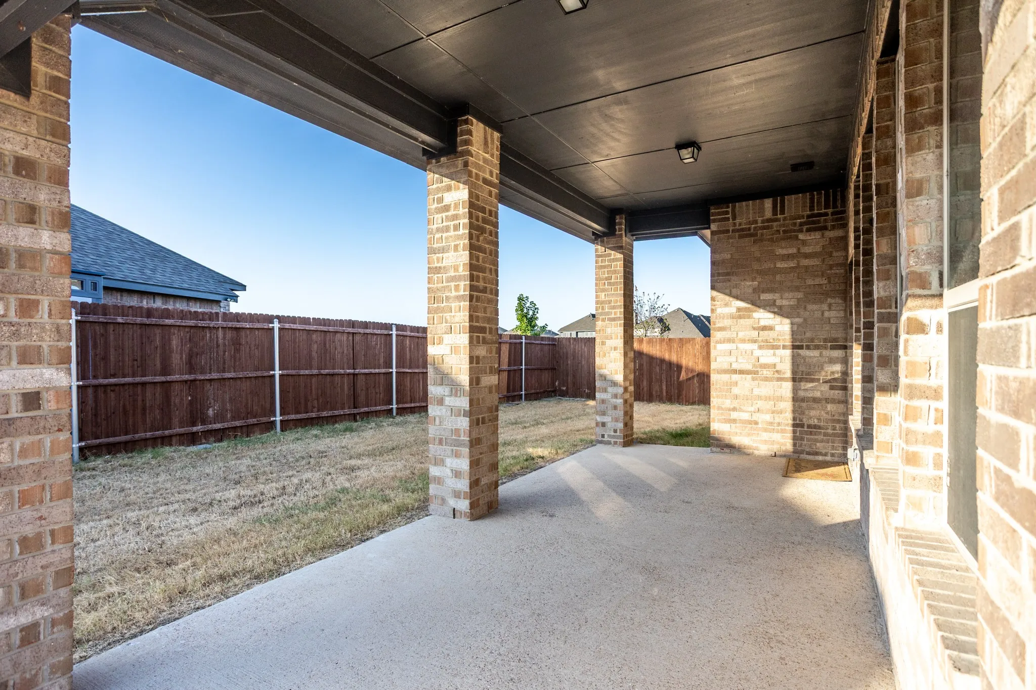 Covered patio with a concrete slab, brick support columns, and an exterior brick wall