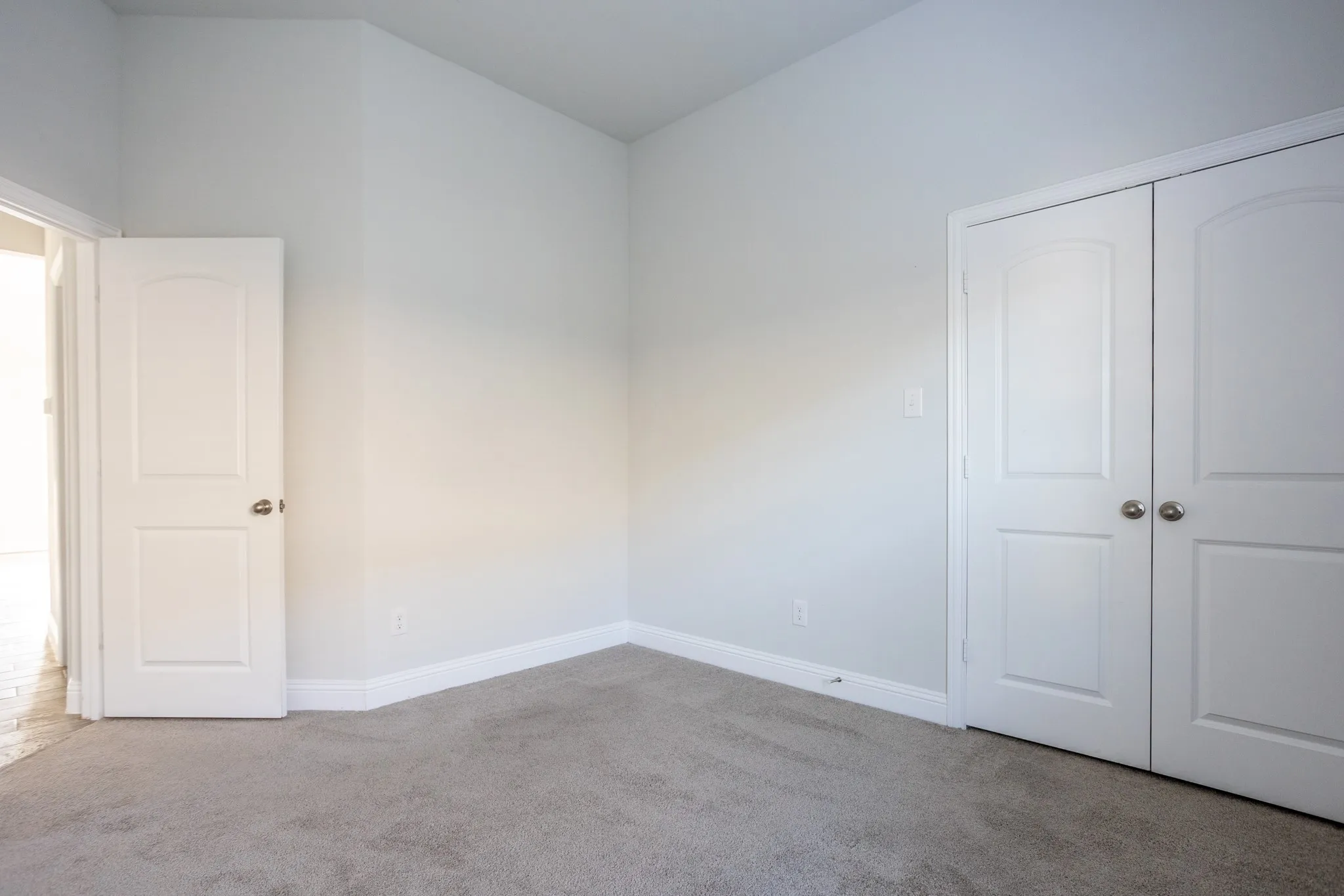 Light gray wall paint, gray carpet flooring, white trim, and white bi-fold closet doors