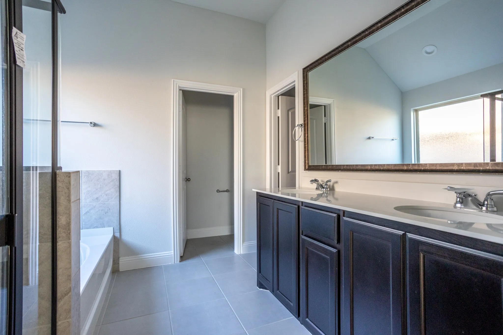 Dual vanity with dark wood cabinetry and integrated sinks, large framed mirror, and tiled flooring