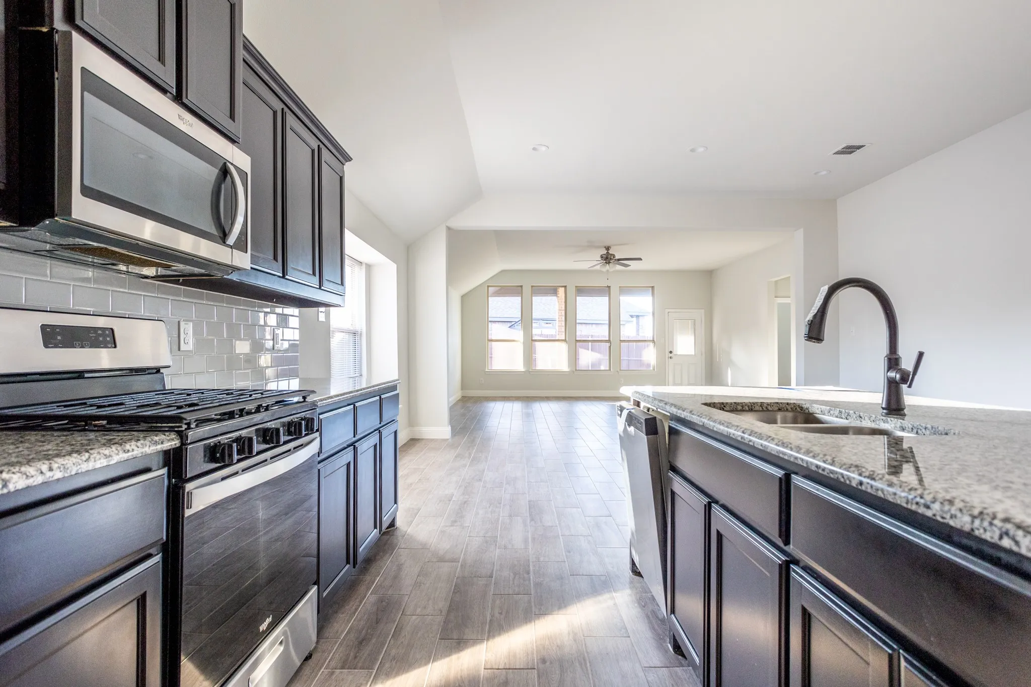 Kitchen featuring granite countertops, stainless steel appliances, dark wood-finish cabinetry, and a subway tile backsplash