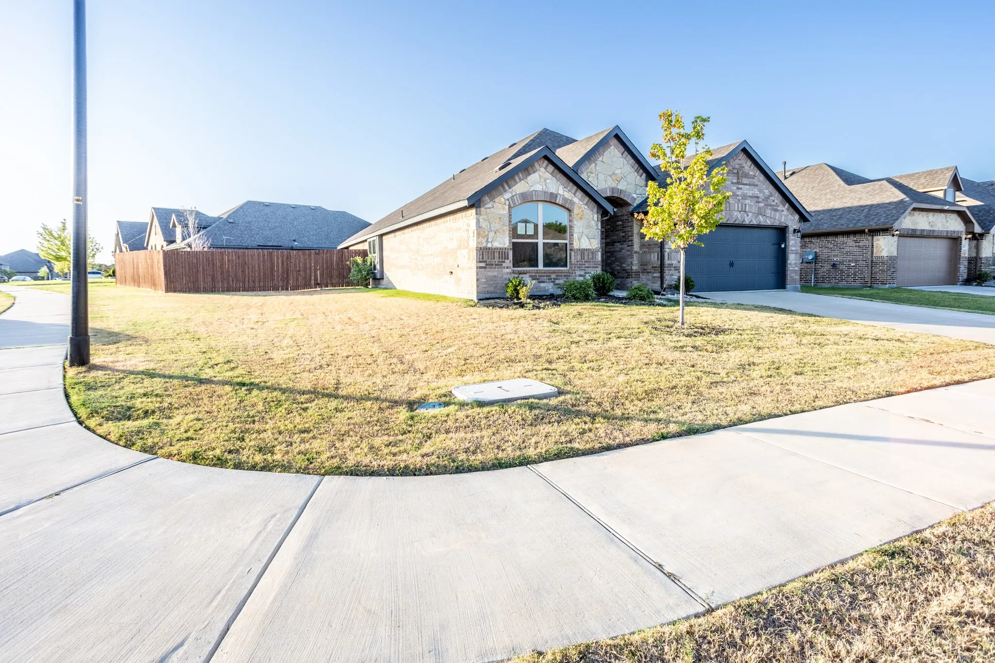 Stone and brick exterior, arched window details, attached garage, concrete sidewalk, fully fenced backyard