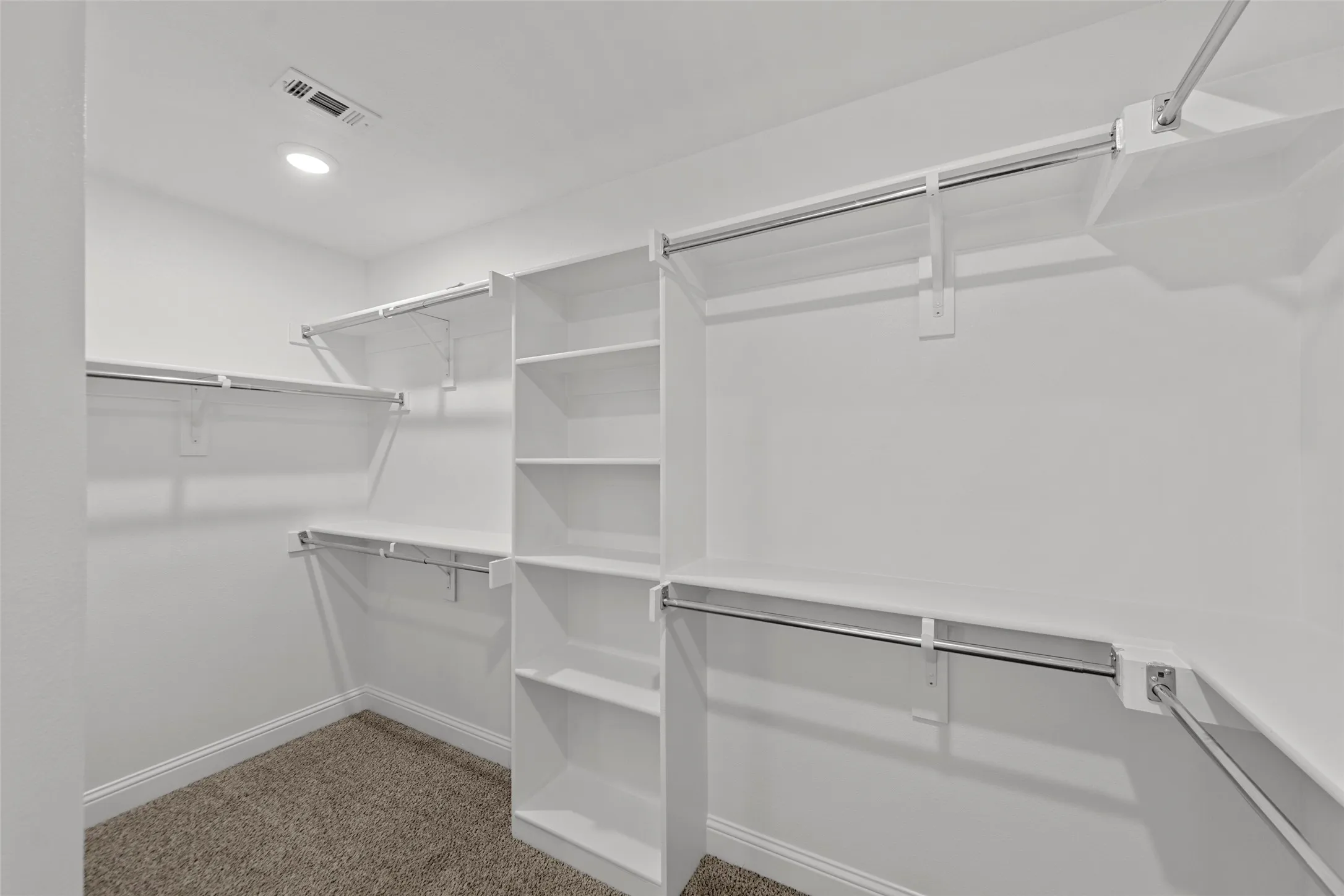 Walk-in closet with integrated shelving, multiple hanging rods, built-in vertical storage, recessed lighting, and carpeted flooring