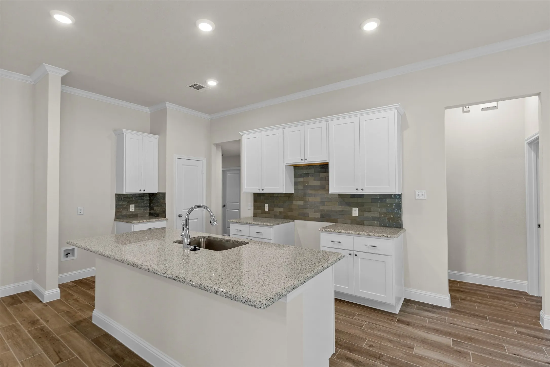 Kitchen featuring a center island with sink, granite-style countertops, white cabinetry, a tiled backsplash, and wood-finish flooring