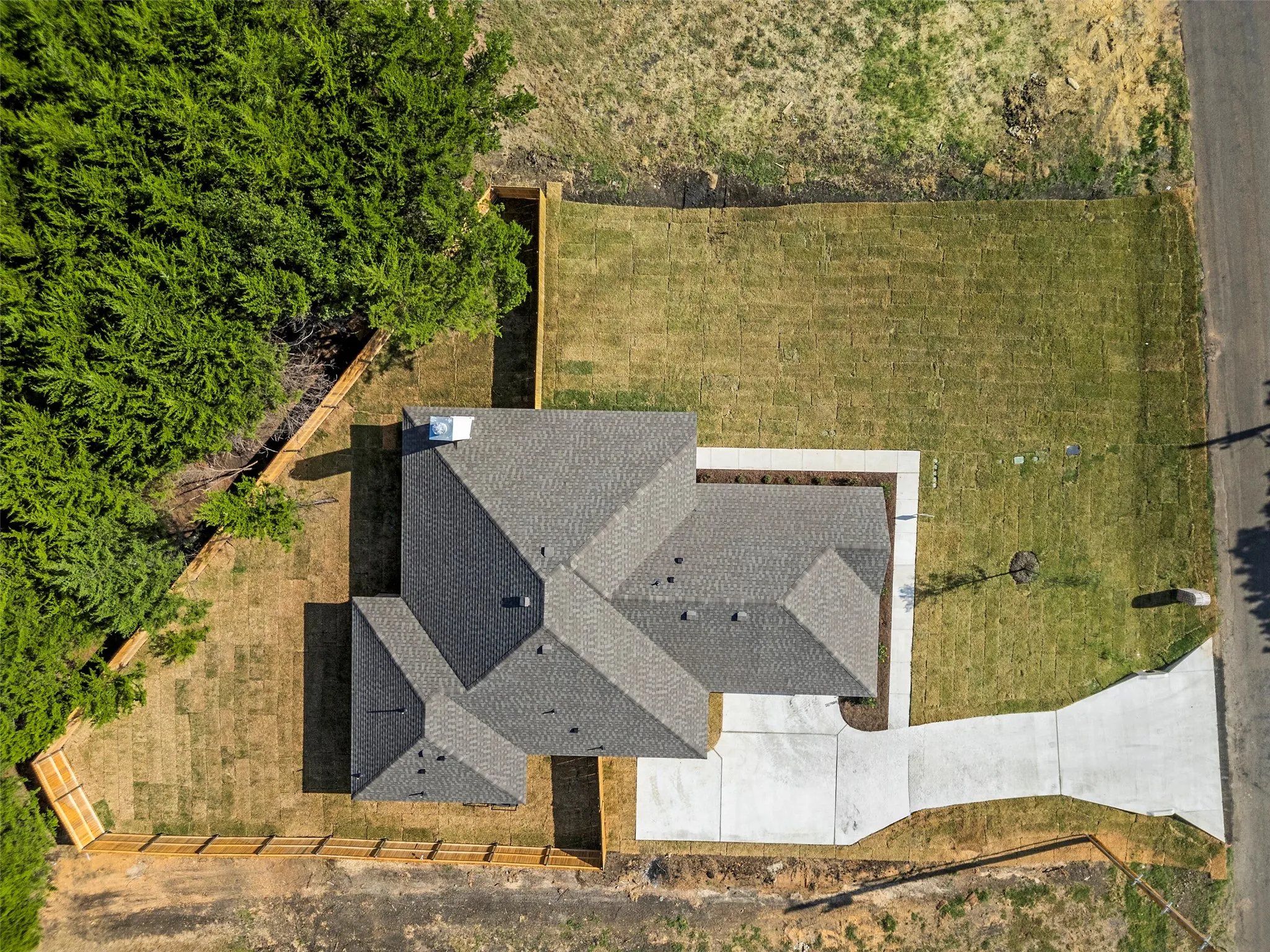 Gable roofline, concrete driveway, concrete sidewalk, fenced perimeter, and established landscaping