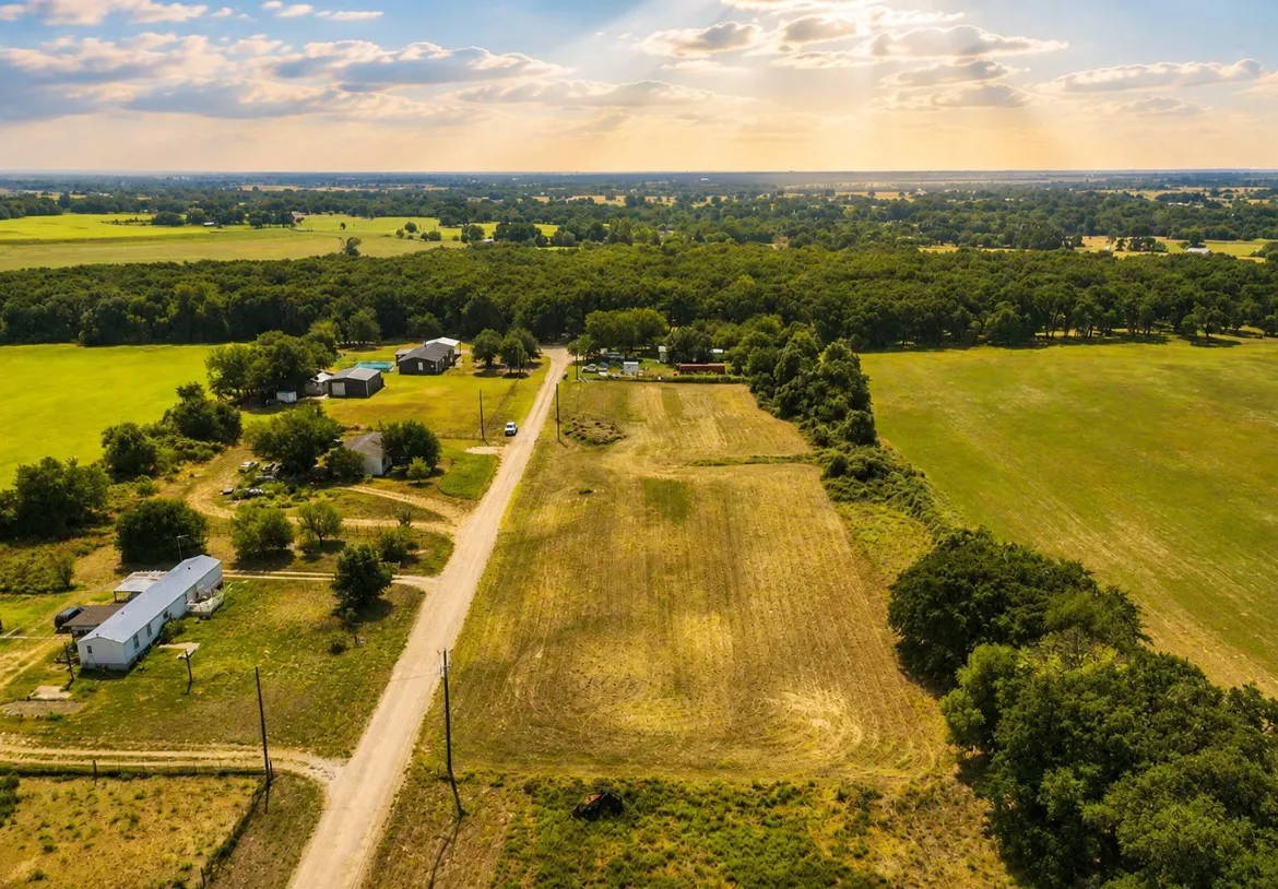 Rural property featuring expansive green fields, mature tree lines, and multiple structures