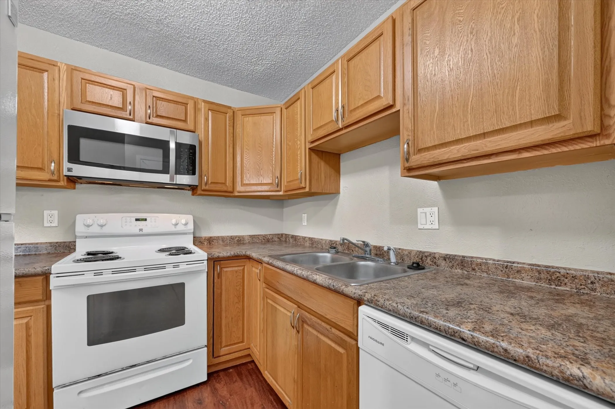 Kitchen featuring wood cabinetry, laminate countertops, a double basin stainless steel sink, and stainless steel microwave