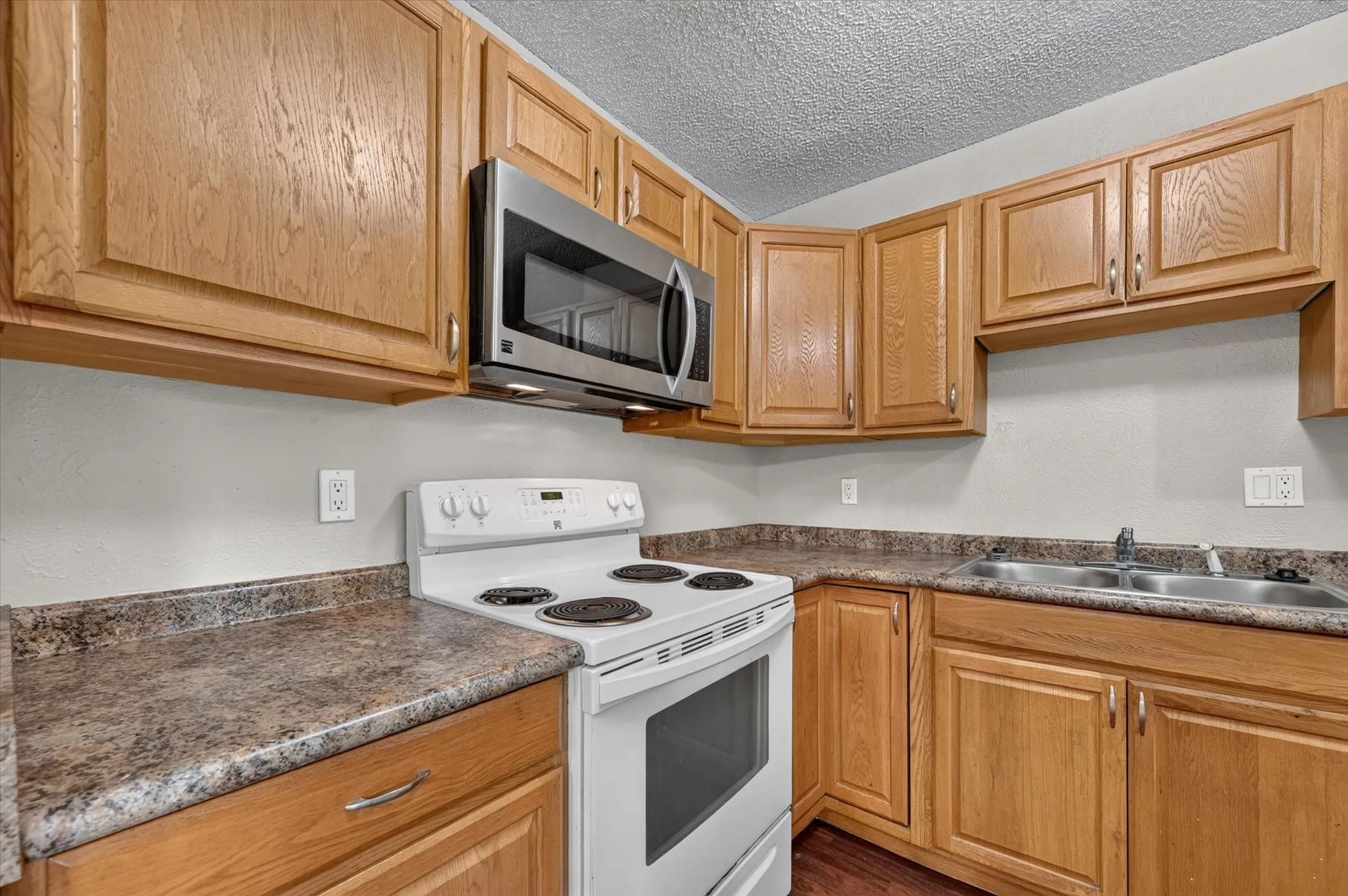Kitchen featuring wood cabinetry, stainless steel microwave, white electric range, and a double basin sink
