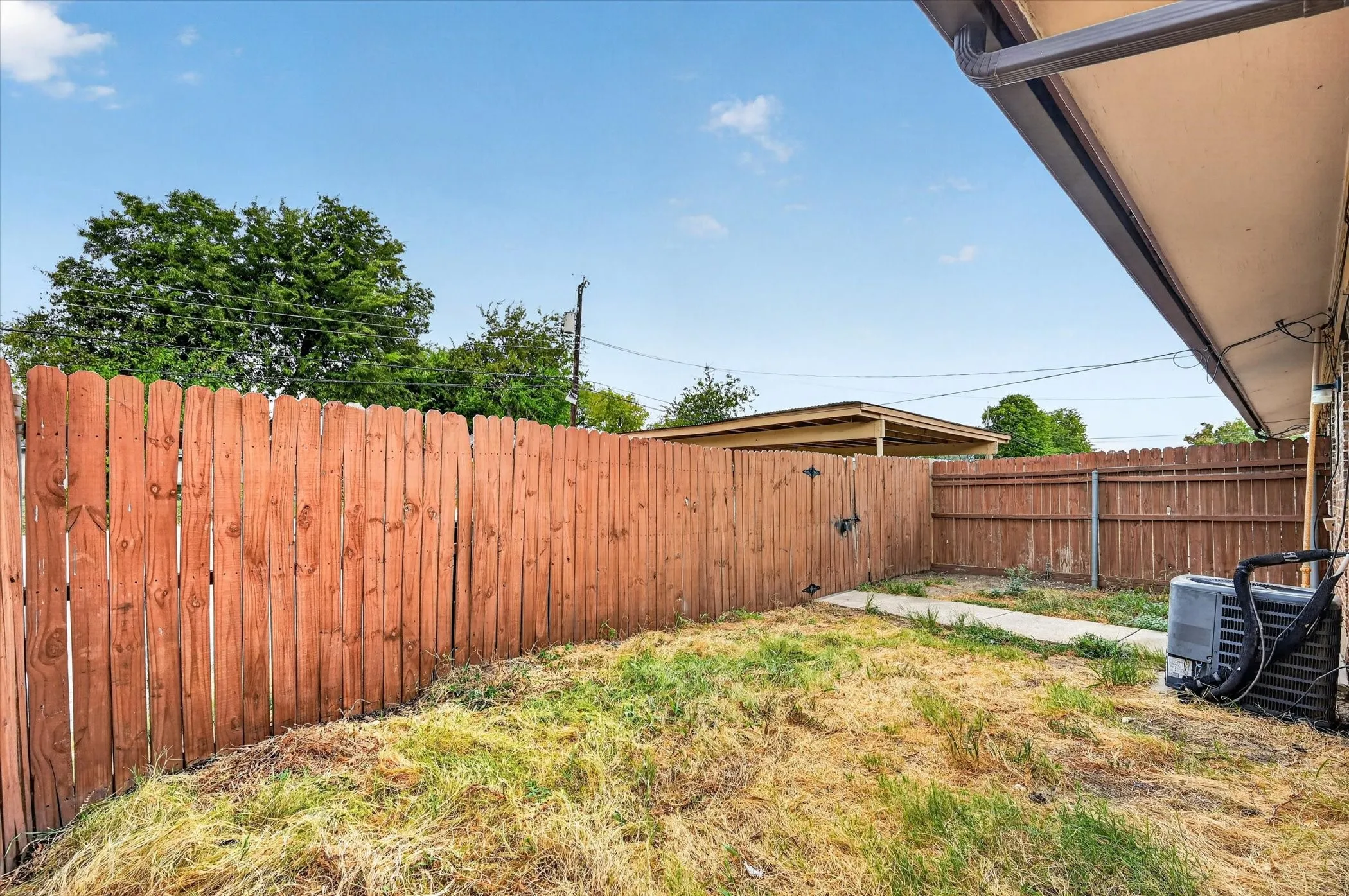 Fenced backyard featuring a concrete walkway, brown wood fence, and rain gutters