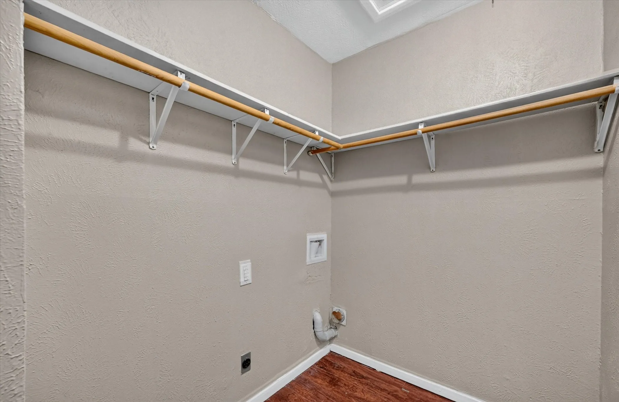 Closet with wood-finish flooring, white baseboards, and built-in shelving with hanging rods
