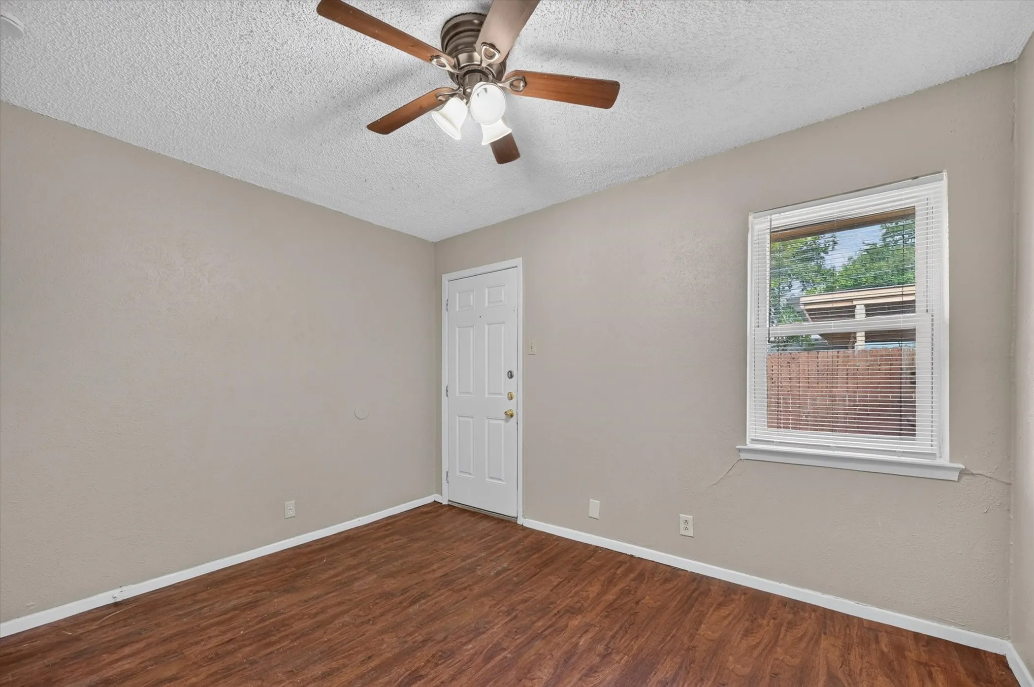 Wood-finish flooring, ceiling fan with integrated lighting, white paneled door, and a window with blinds