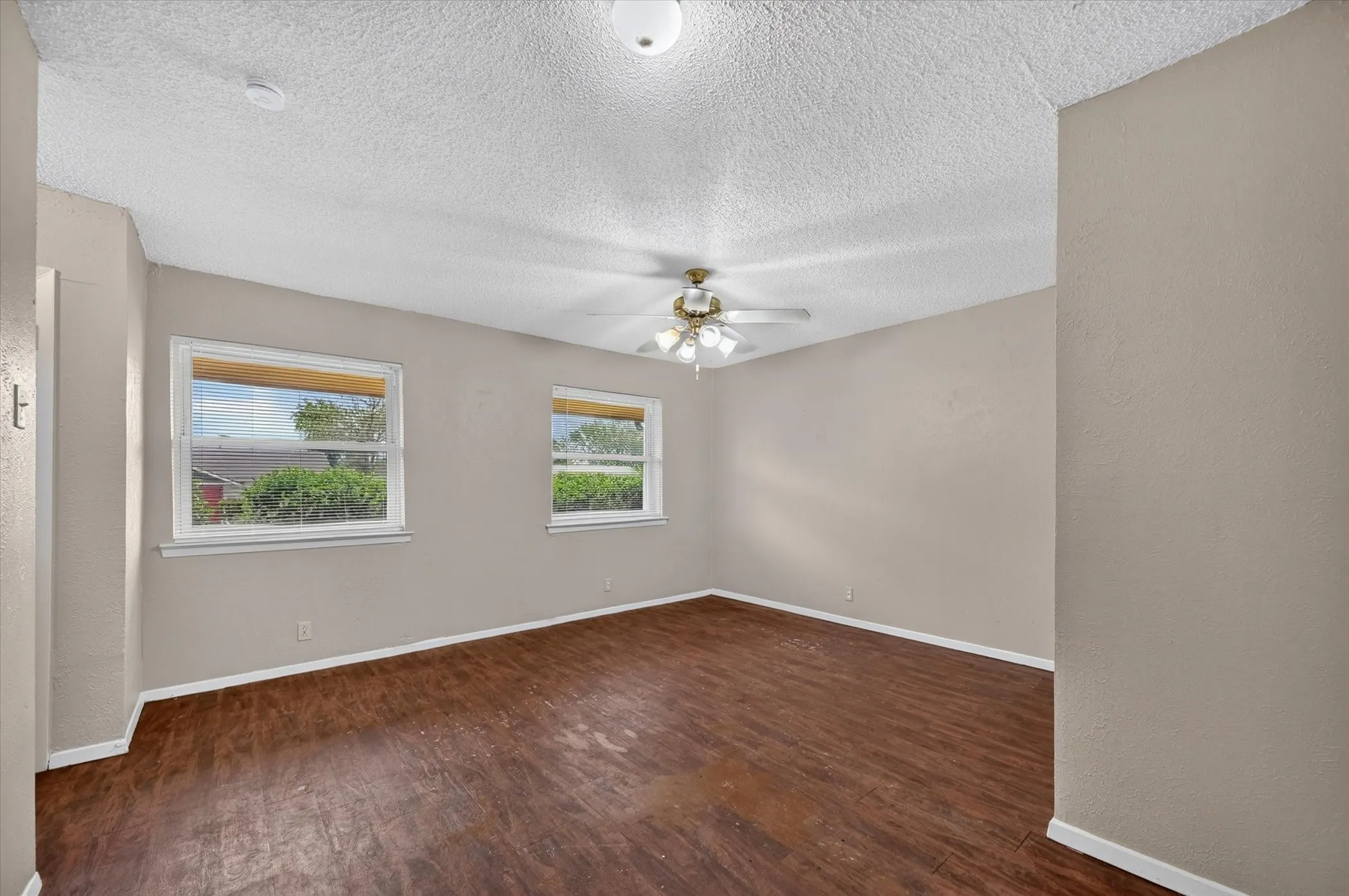 Wood-finish flooring, neutral wall tones, two windows with white trim, and a ceiling fan with integrated lighting