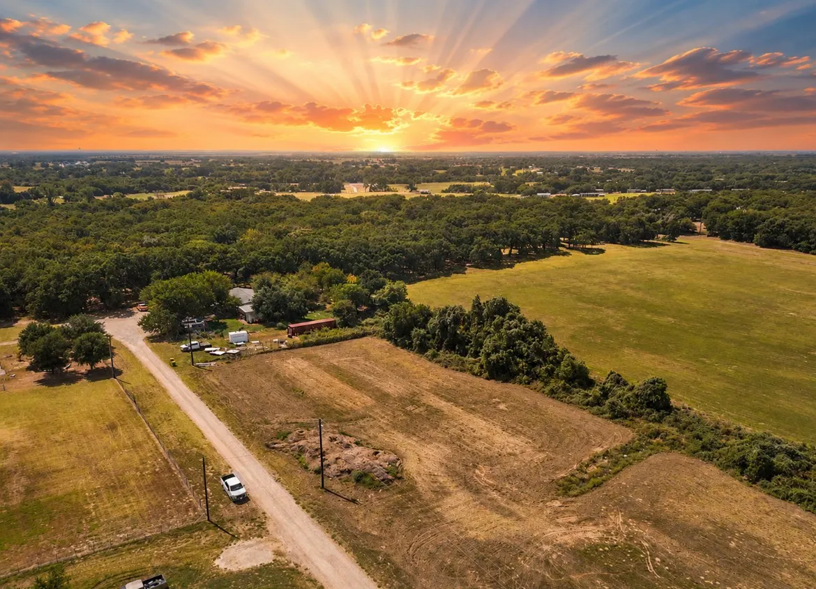 Expansive rural property featuring a gravel driveway, open fields, and mature tree lines