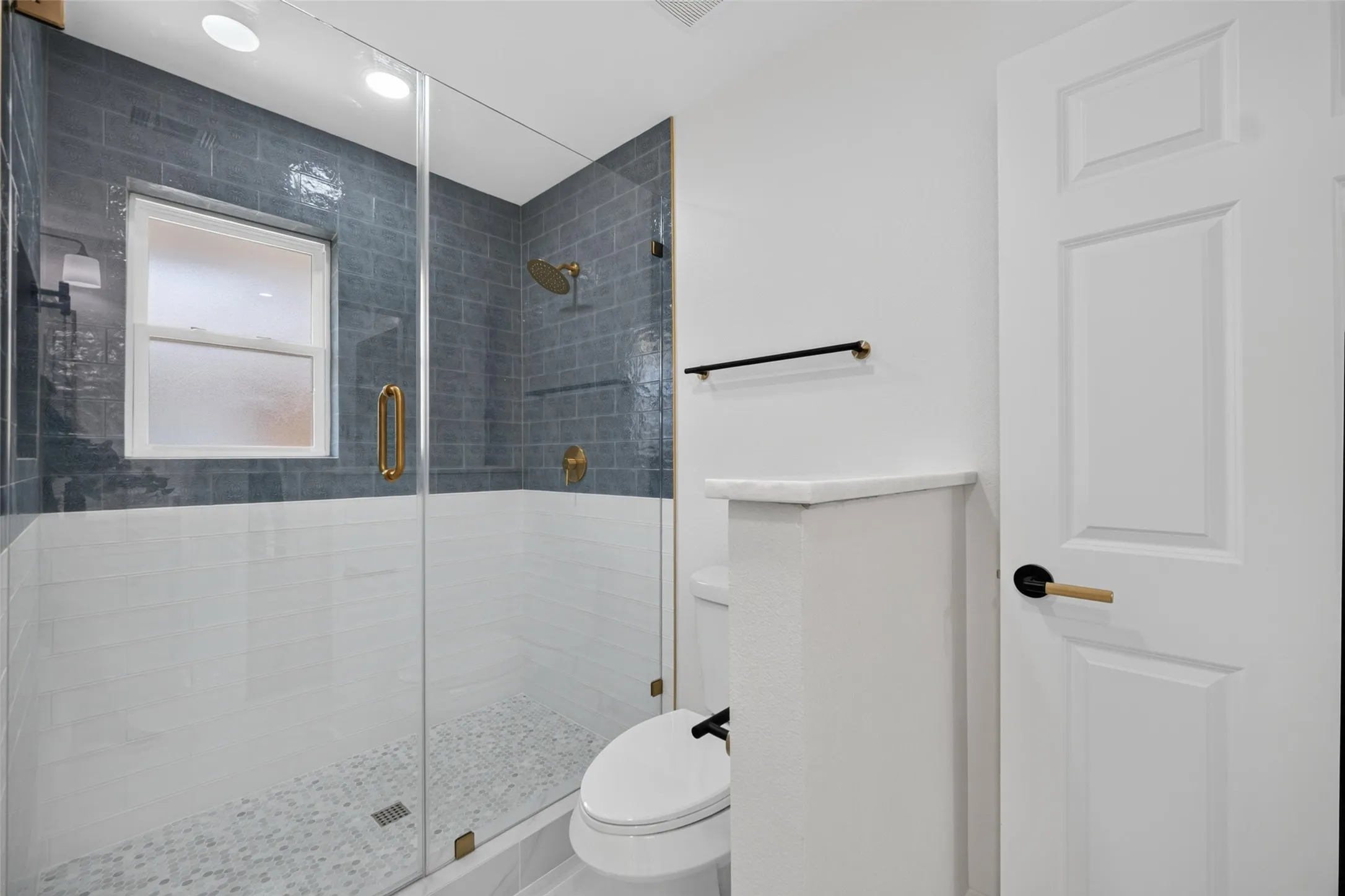 Glass-enclosed shower with gold-tone fixtures, subway tile surround, and mosaic tile flooring