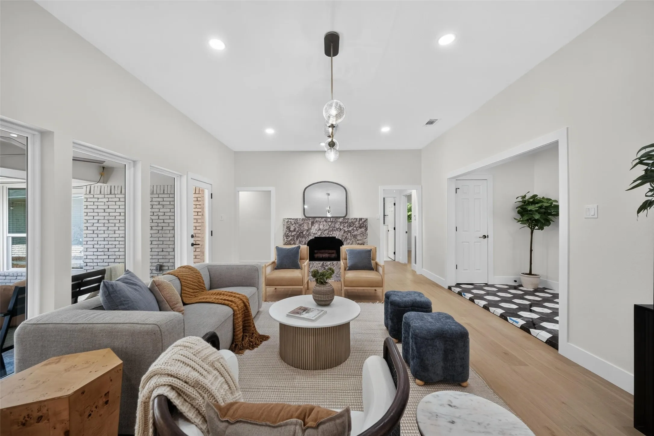 Vaulted ceilings with recessed lighting, light wood-finish flooring, a fireplace featuring a stone surround, and multiple glass panel doors providing access to an outdoor area