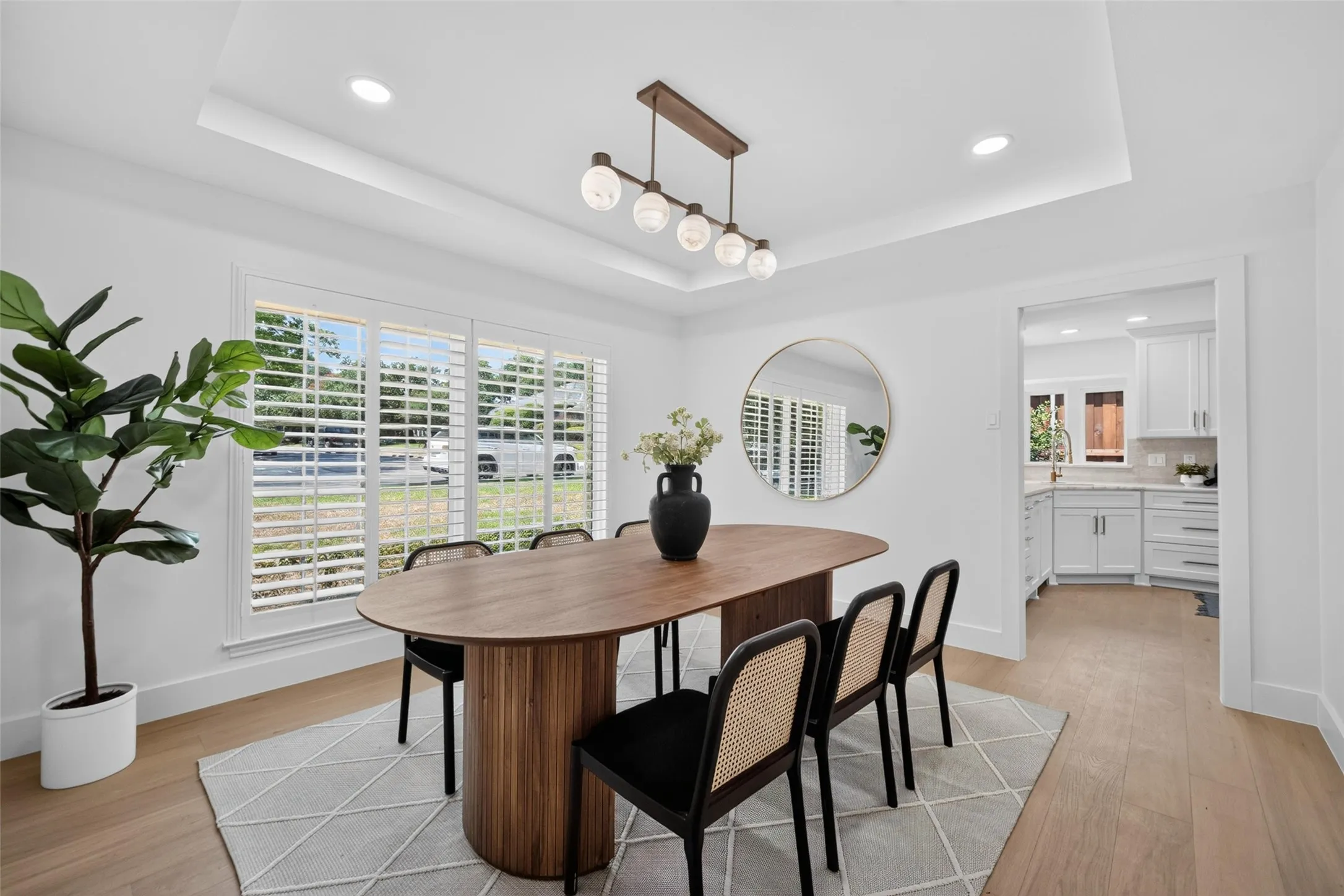 Tray ceiling with recessed lighting, wood-finish flooring, plantation shutters, and a kitchen pass-through
