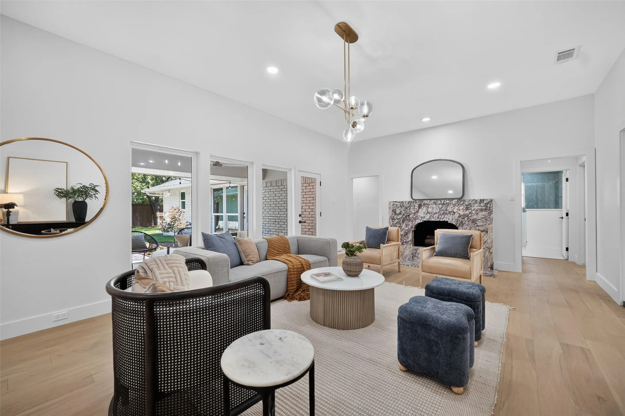 Spacious living area featuring high ceilings, wood-finish flooring, recessed lighting, a stone-clad fireplace, and multiple large windows overlooking the backyard