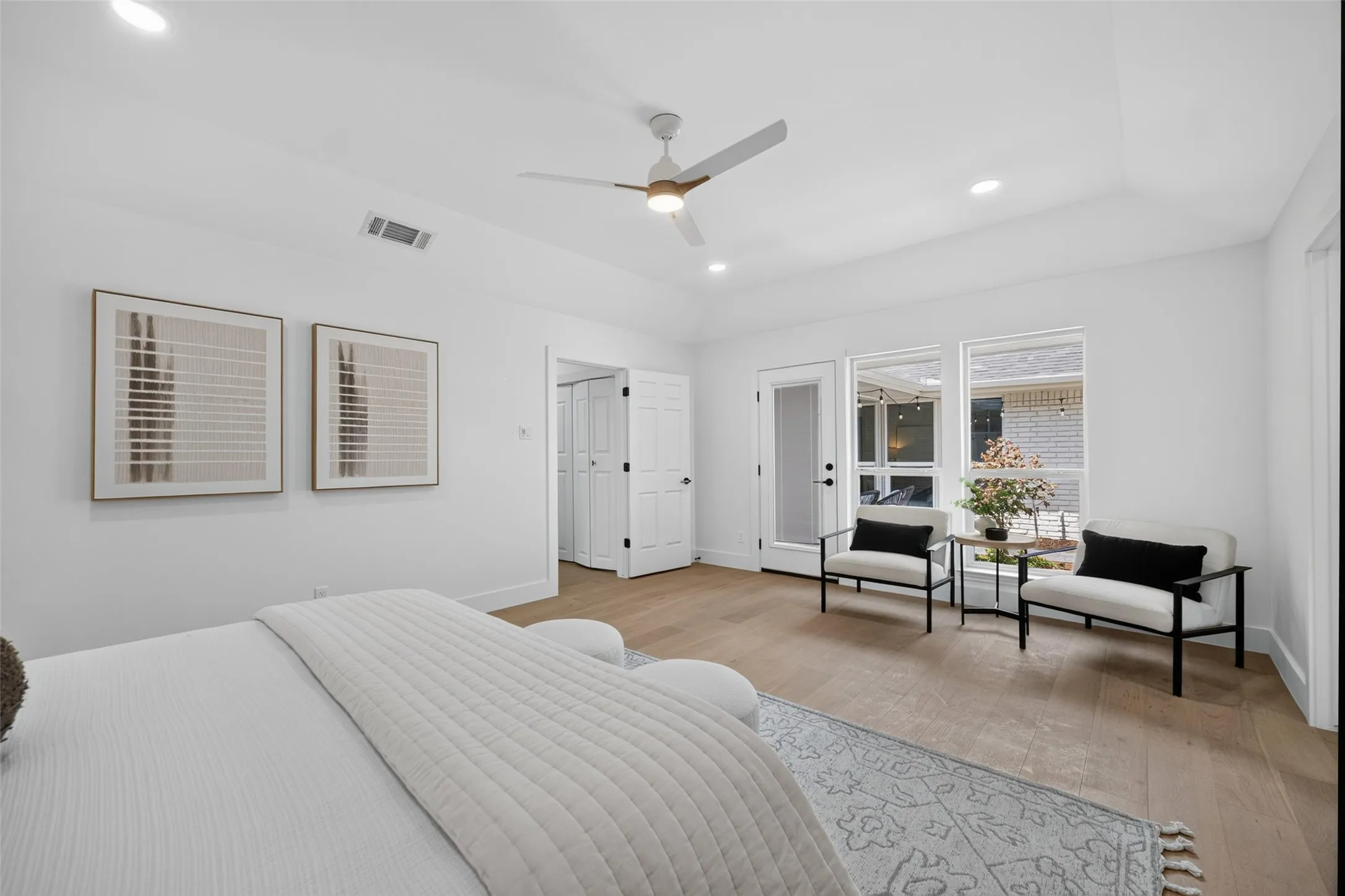 Spacious primary bedroom with wood-finish flooring, ceiling fan, and abundant natural light from expansive multi-pane windows