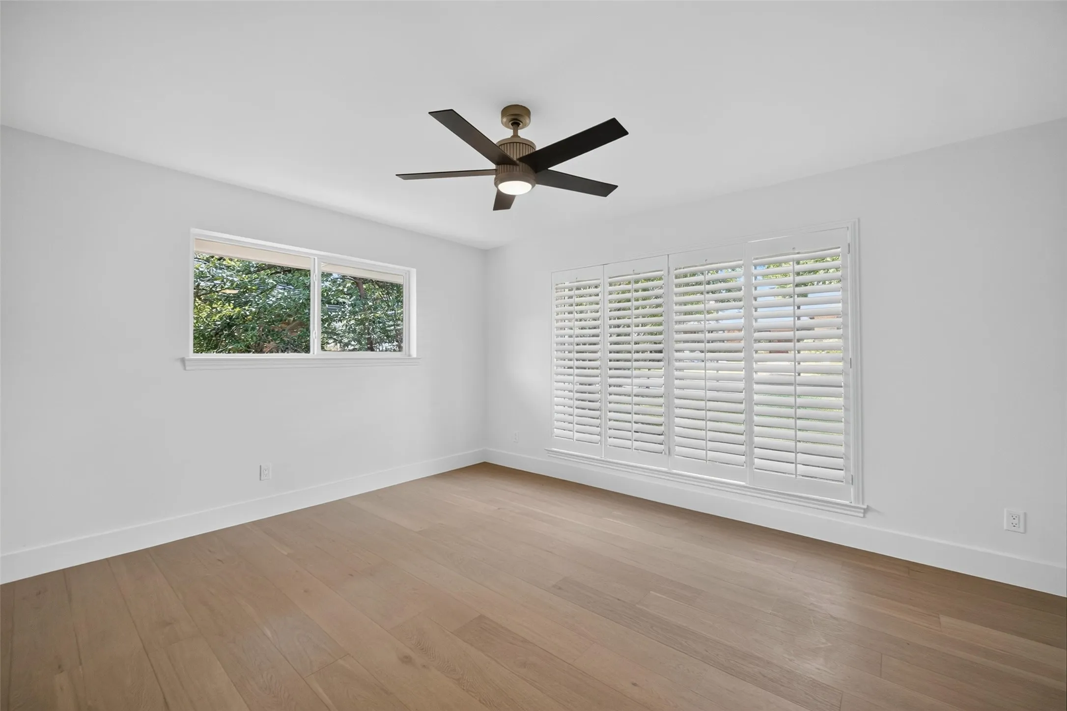 Wood-finish flooring, white walls, ceiling fan with integrated lighting, and window with plantation shutters