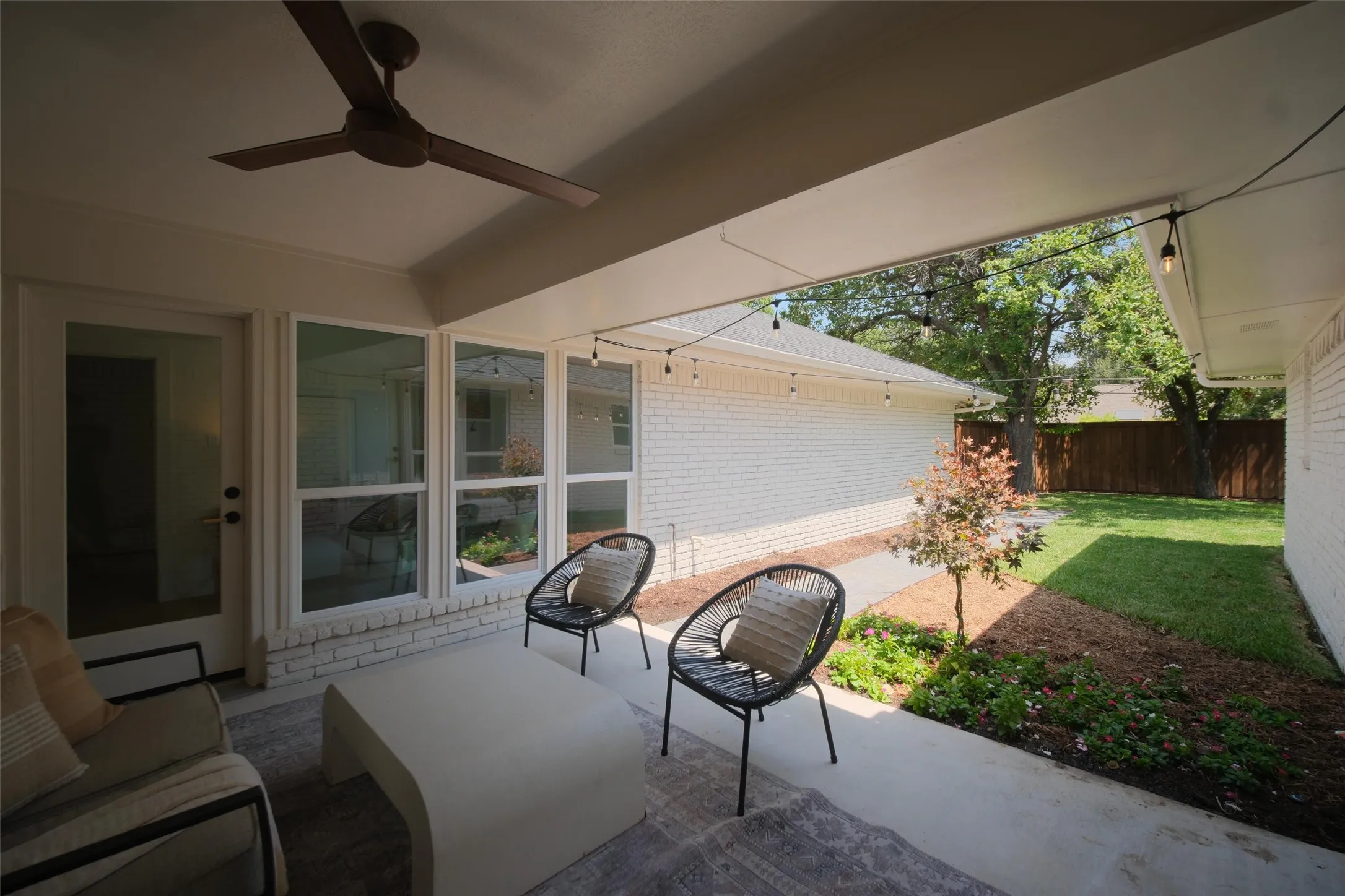 Covered patio featuring a ceiling fan, string lighting, and direct access to the backyard through multiple windows and a glass-paneled door