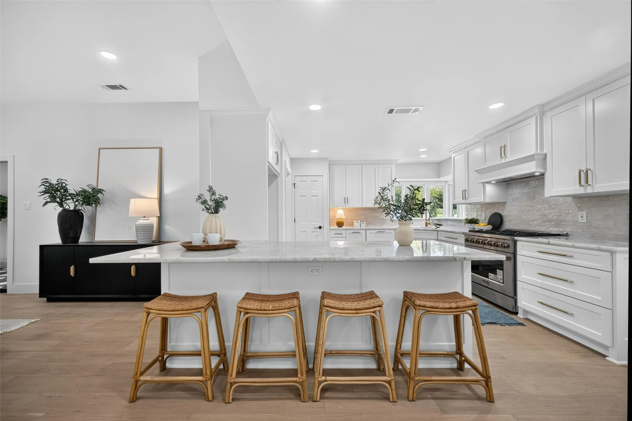 Spacious kitchen featuring an expansive island with stone countertops, white shaker cabinetry, stainless steel range, and wood-finish flooring