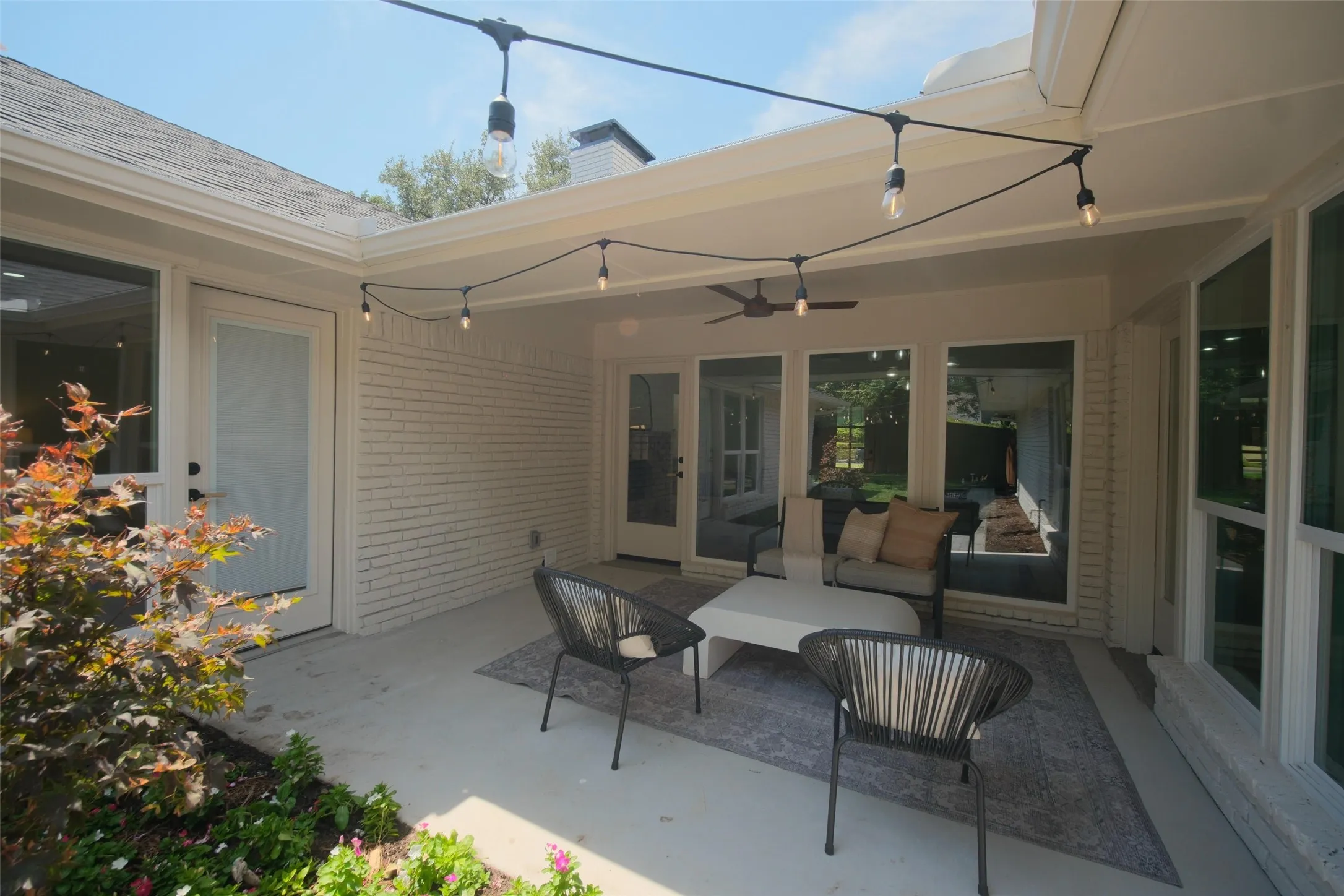 Covered patio with string lighting, a ceiling fan, and painted brick siding