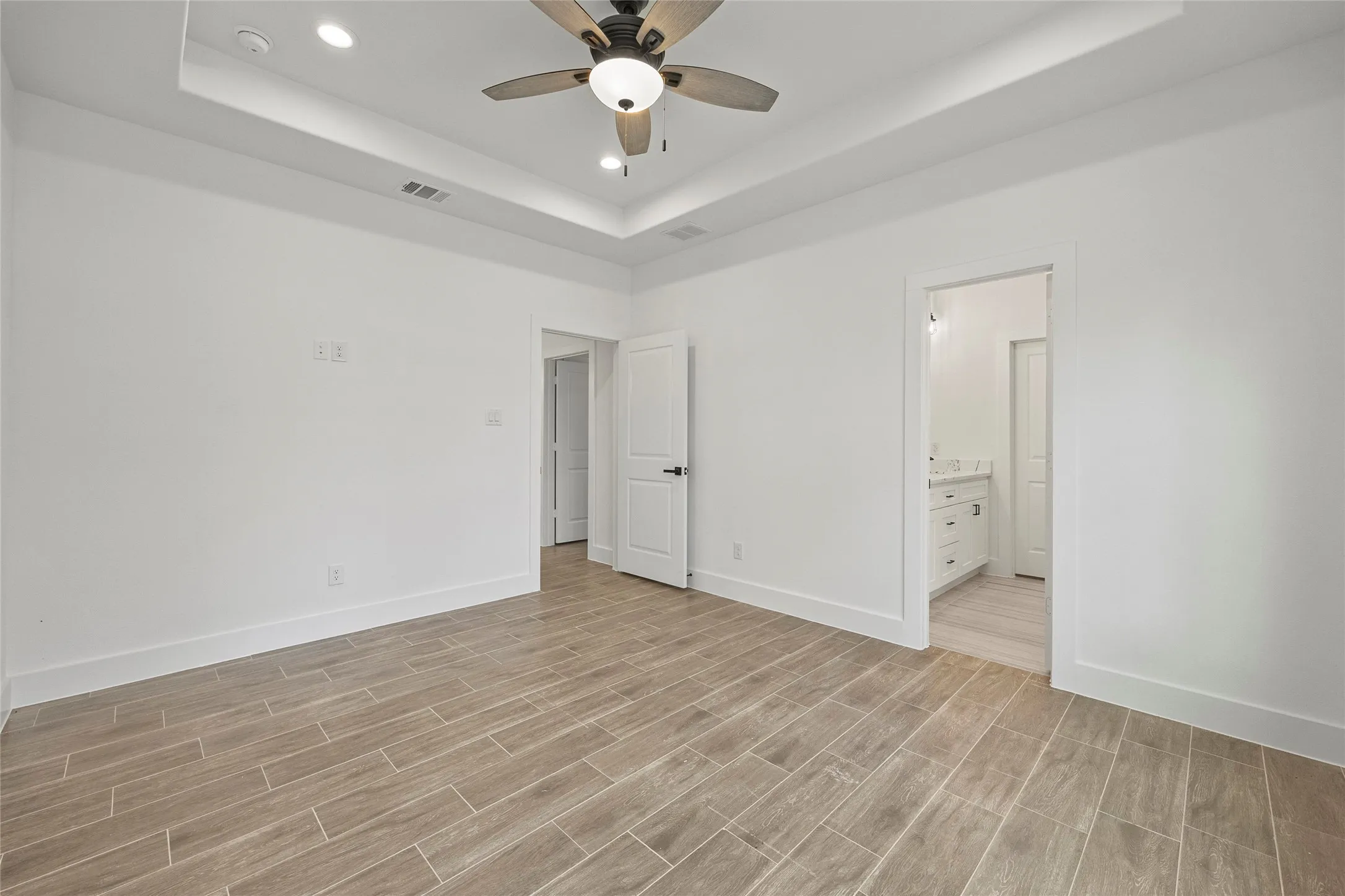 Tray ceiling with recessed lighting and a ceiling fan, wood-finish tile flooring, and white walls