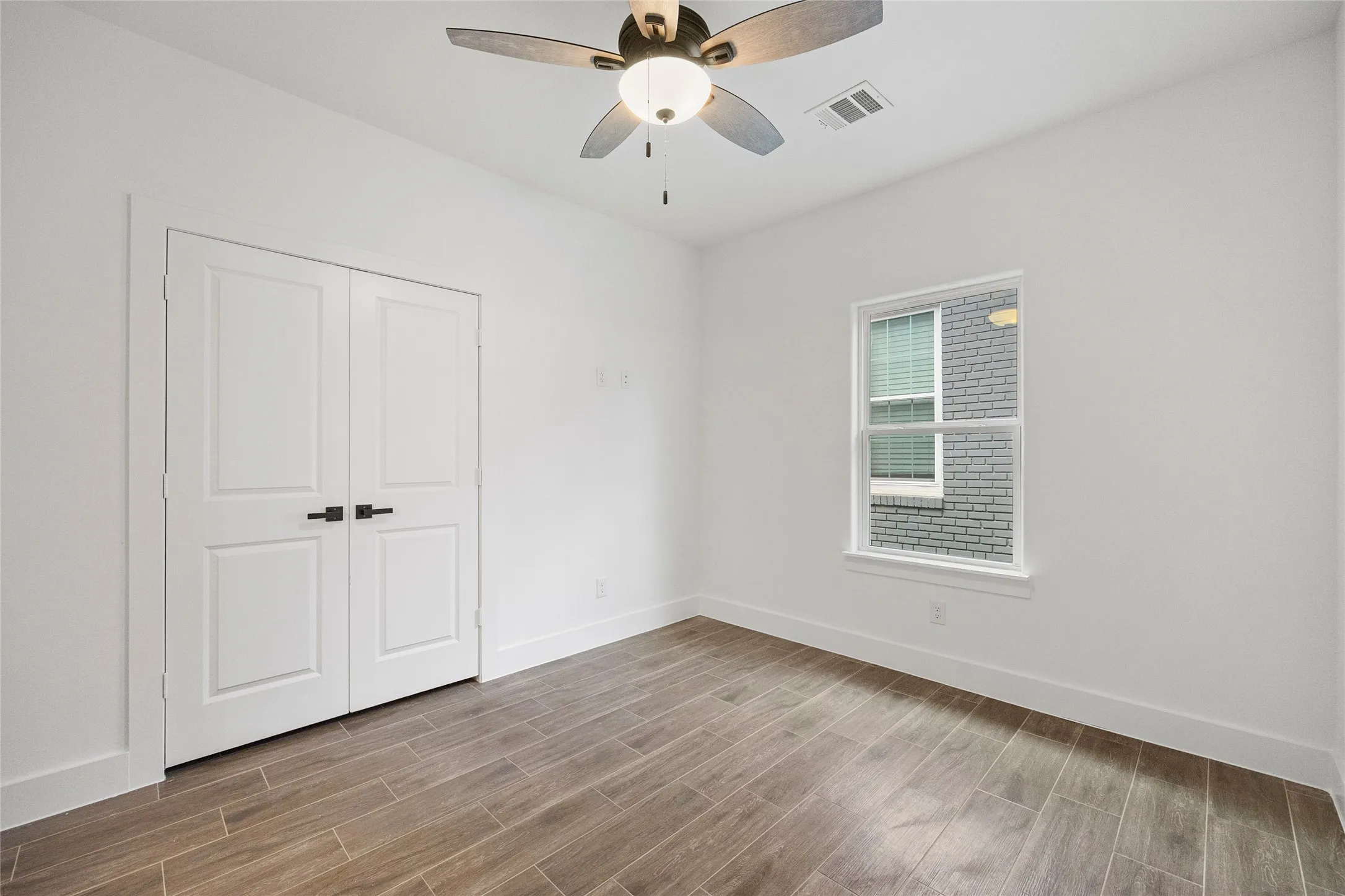 Wood-finish flooring, white walls, double panel doors, ceiling fan with integrated lighting, and a single window