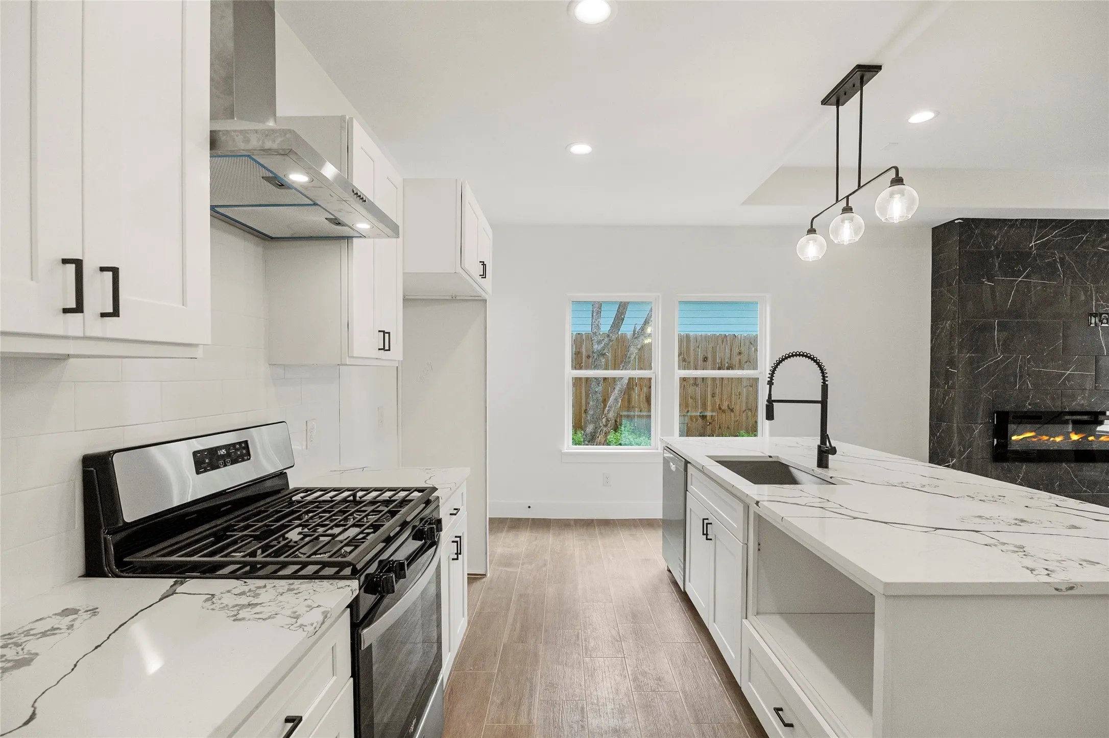 White shaker cabinetry, quartz countertops, stainless steel appliances, wood-finish flooring, and a modern fireplace