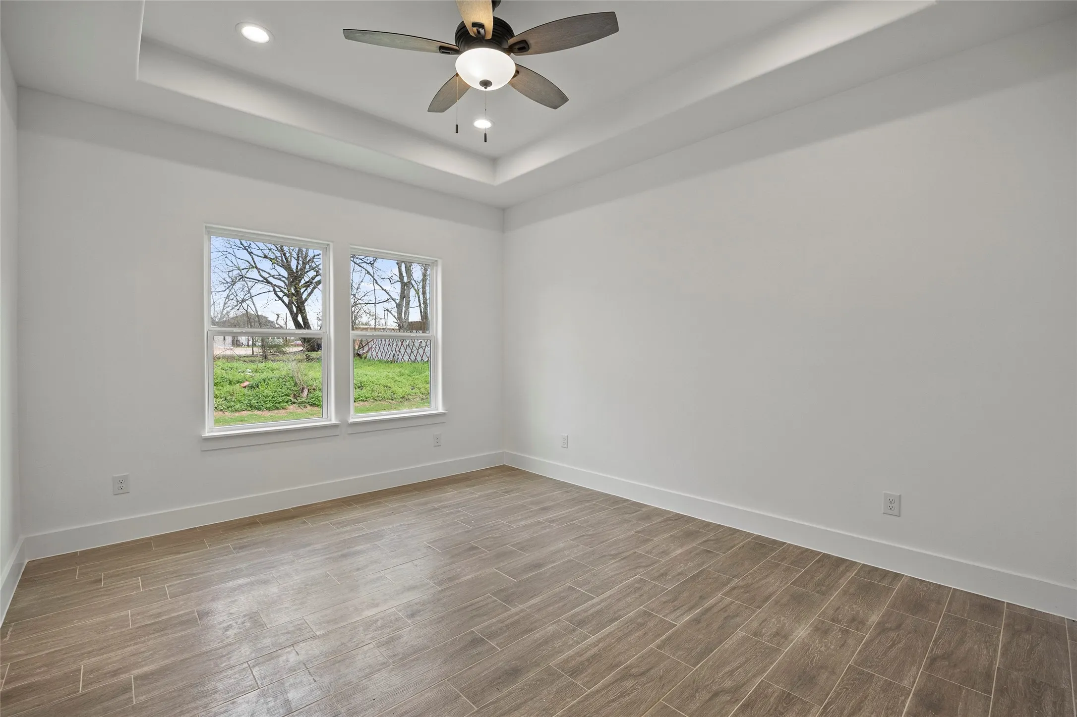 Bright, light-filled bedroom showcasing wood-finish flooring, recessed ceiling lighting, and a ceiling fan with integrated light fixture