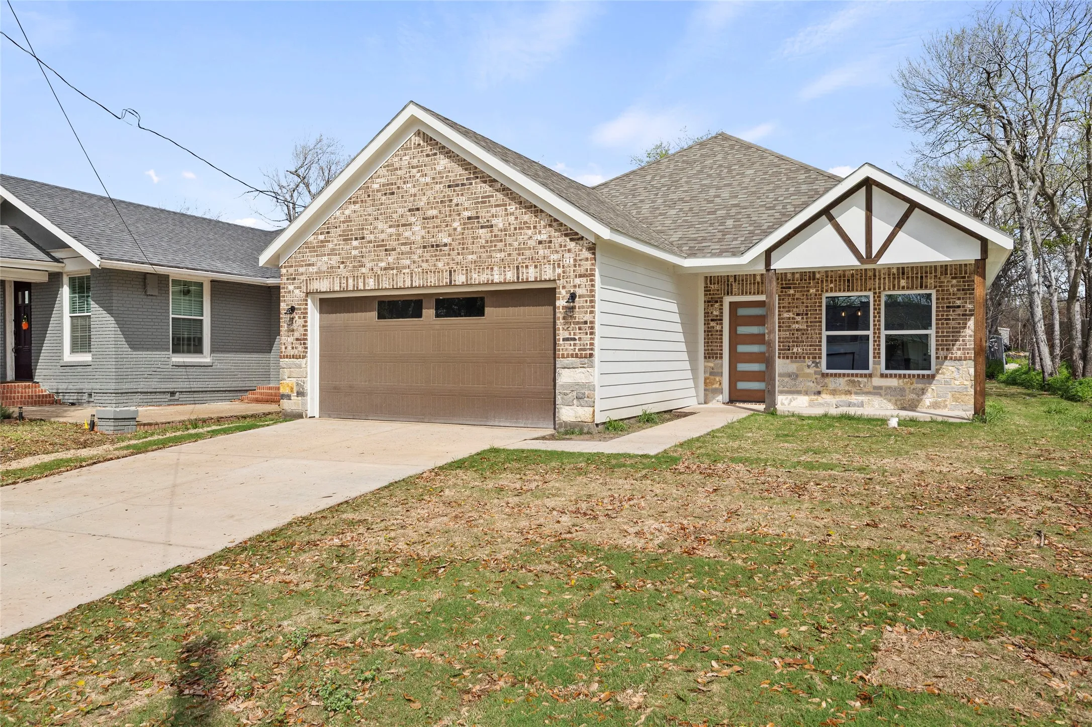Brick and stone façade with siding accents, attached garage, covered entry, and a wood-finish front door with frosted glass panels