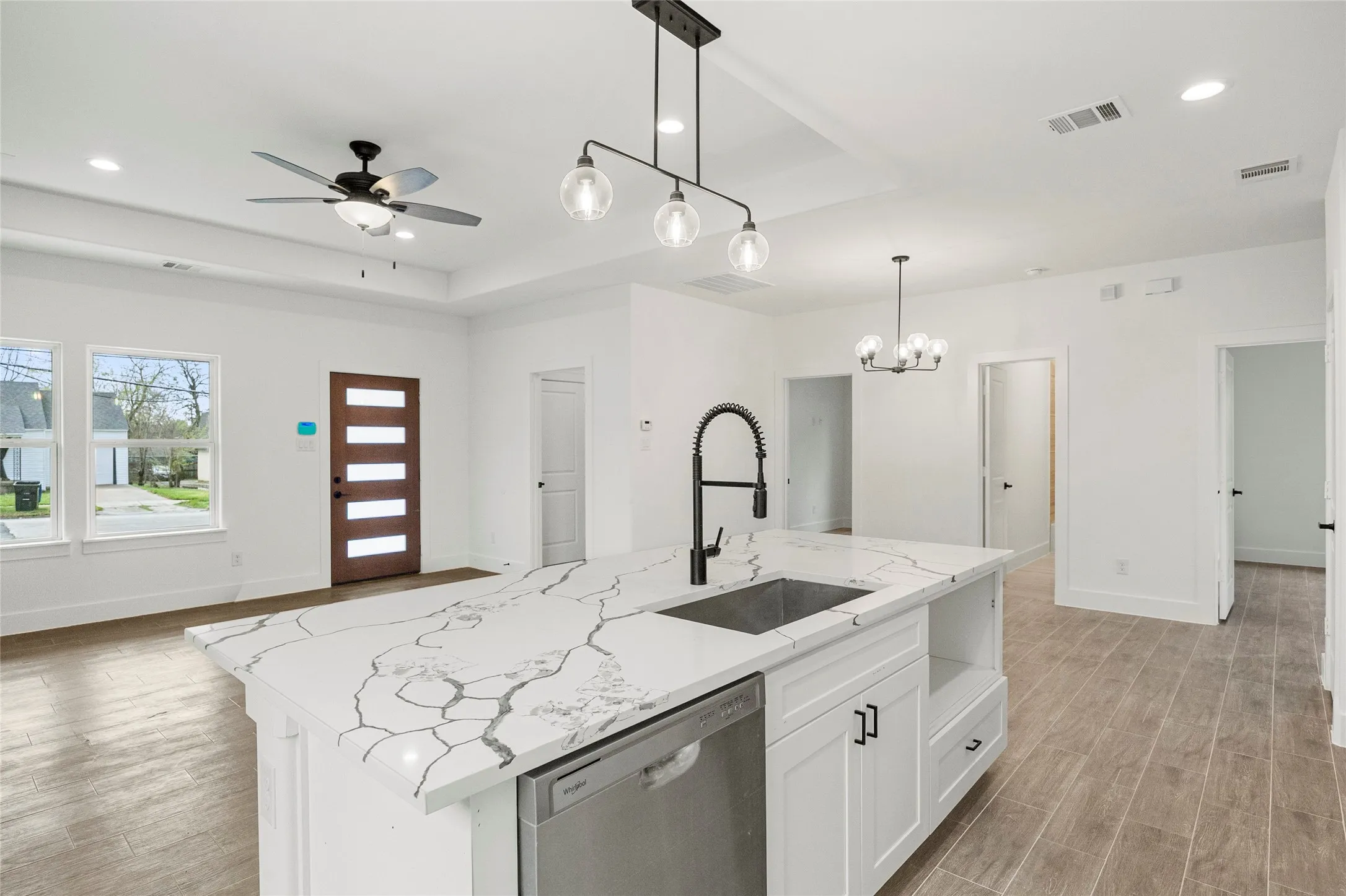 Expansive kitchen island with a stone countertop and integrated sink, stainless steel dishwasher, wood-finish flooring, and contemporary pendant lighting