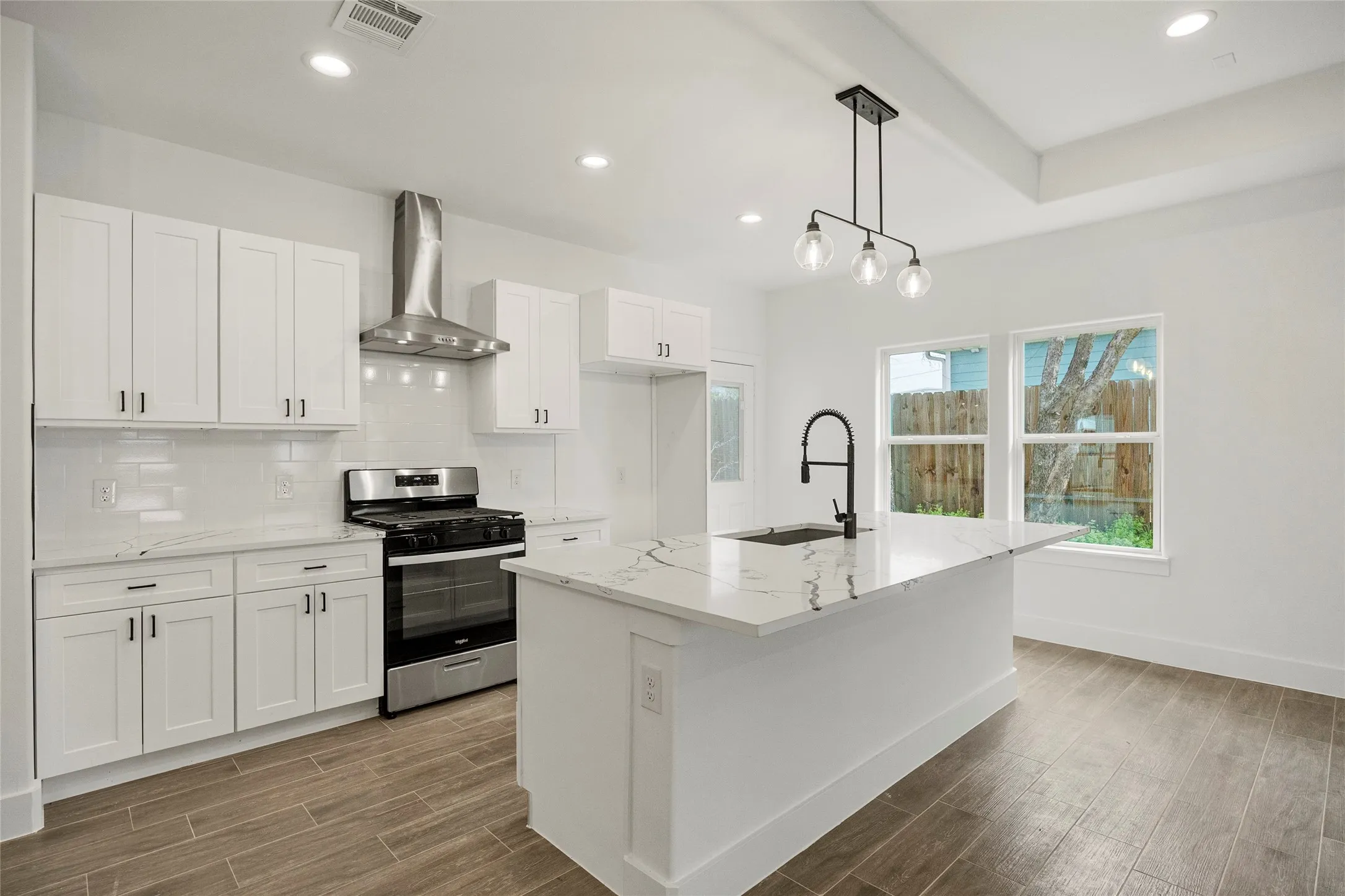 Contemporary kitchen featuring white cabinetry, stainless steel appliances, a center island with sink, quartz countertops, and wood-finish flooring