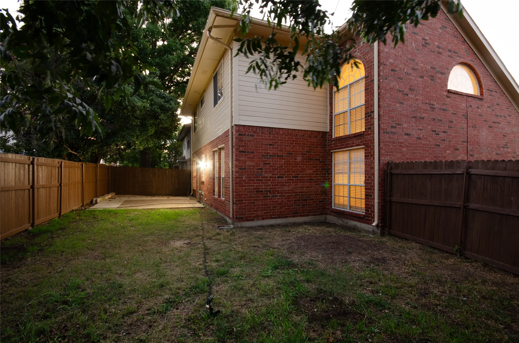 Brick exterior with an arched window, multiple large windows, and a privacy fence