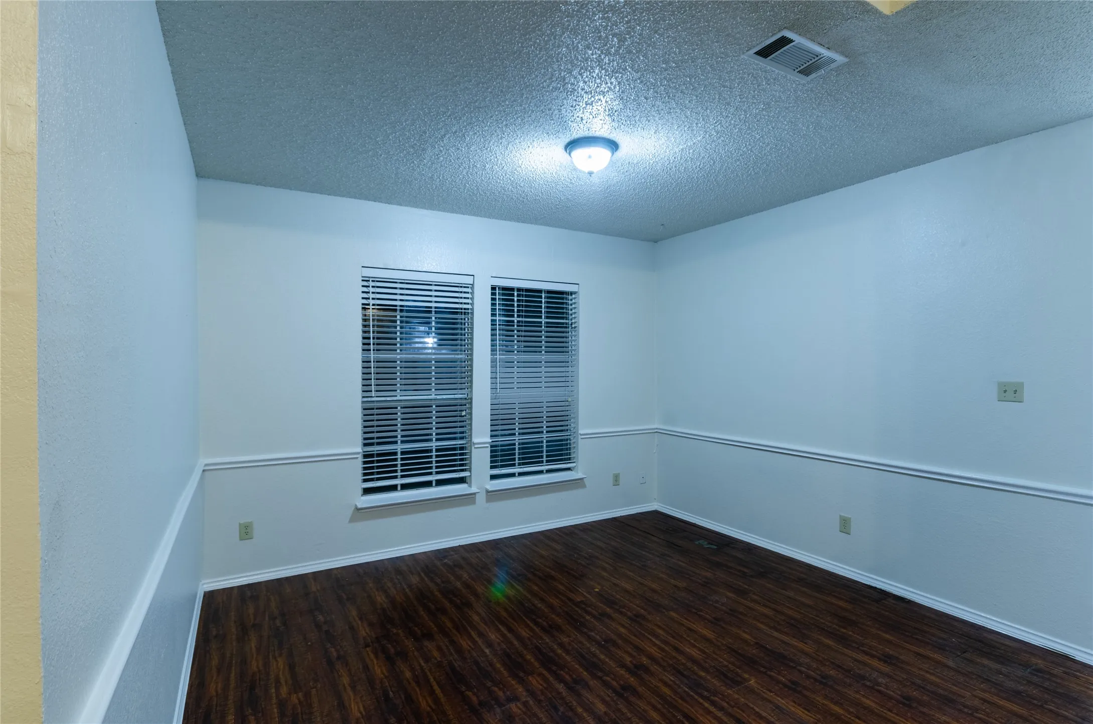 Dining room with wood-finish flooring, white walls, two windows with blinds, and decorative chair rail molding