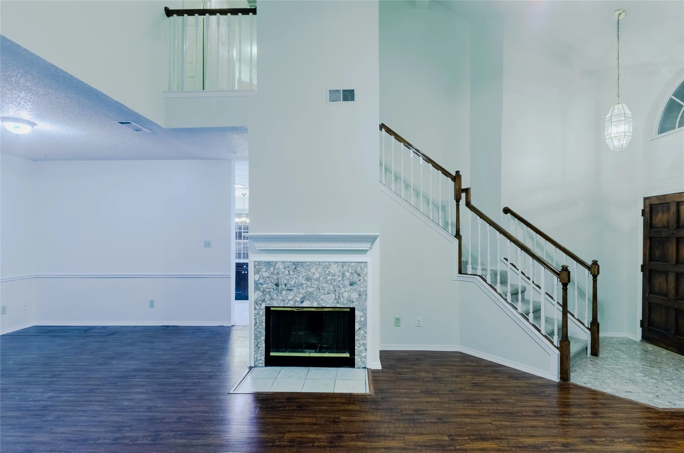 Two-story living area featuring wood-finish flooring, a fireplace with a stone surround, and a staircase with wood handrails