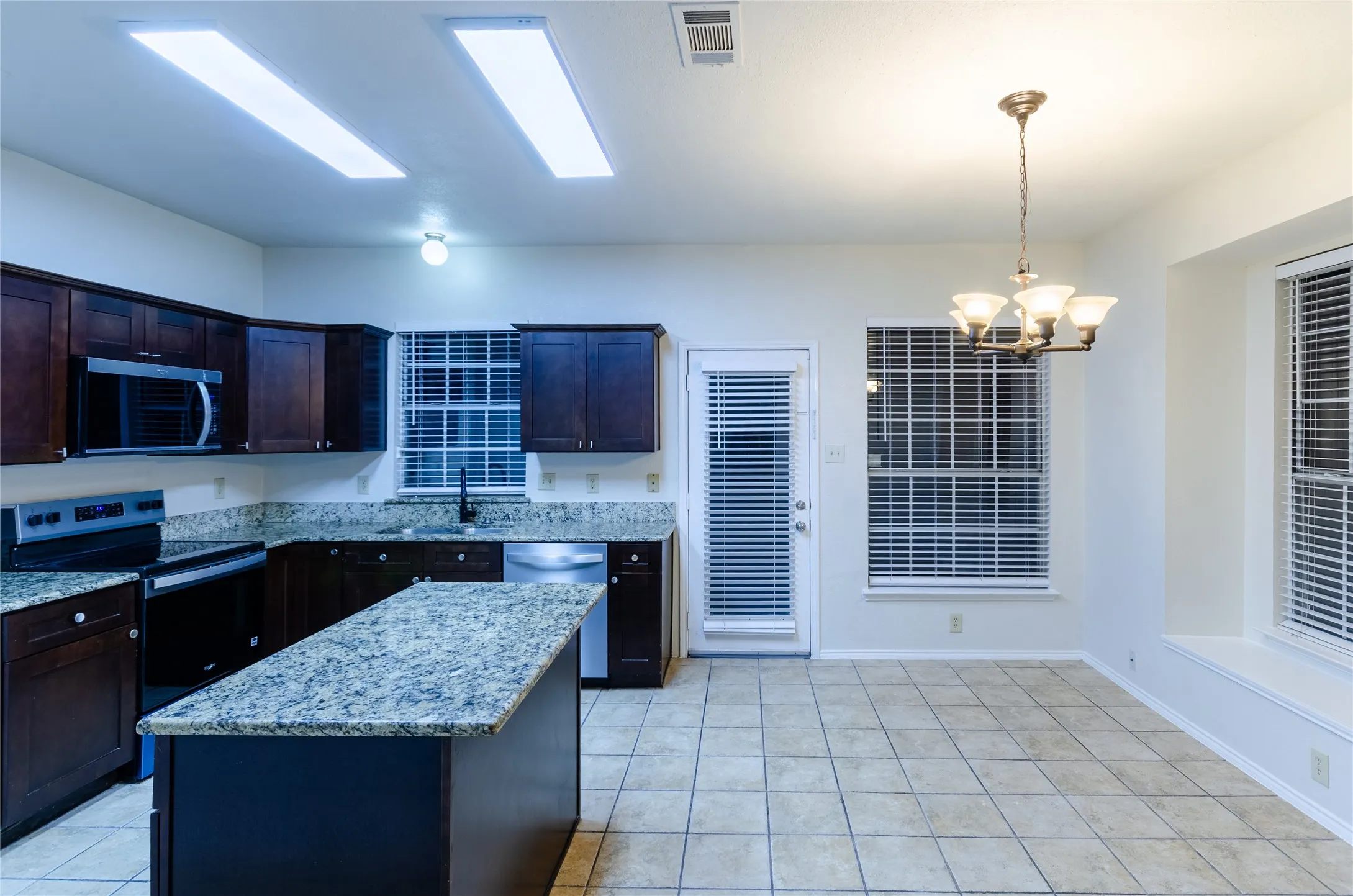 Kitchen featuring dark wood-finish cabinetry, light-toned granite countertops, a central island, and stainless steel appliances
