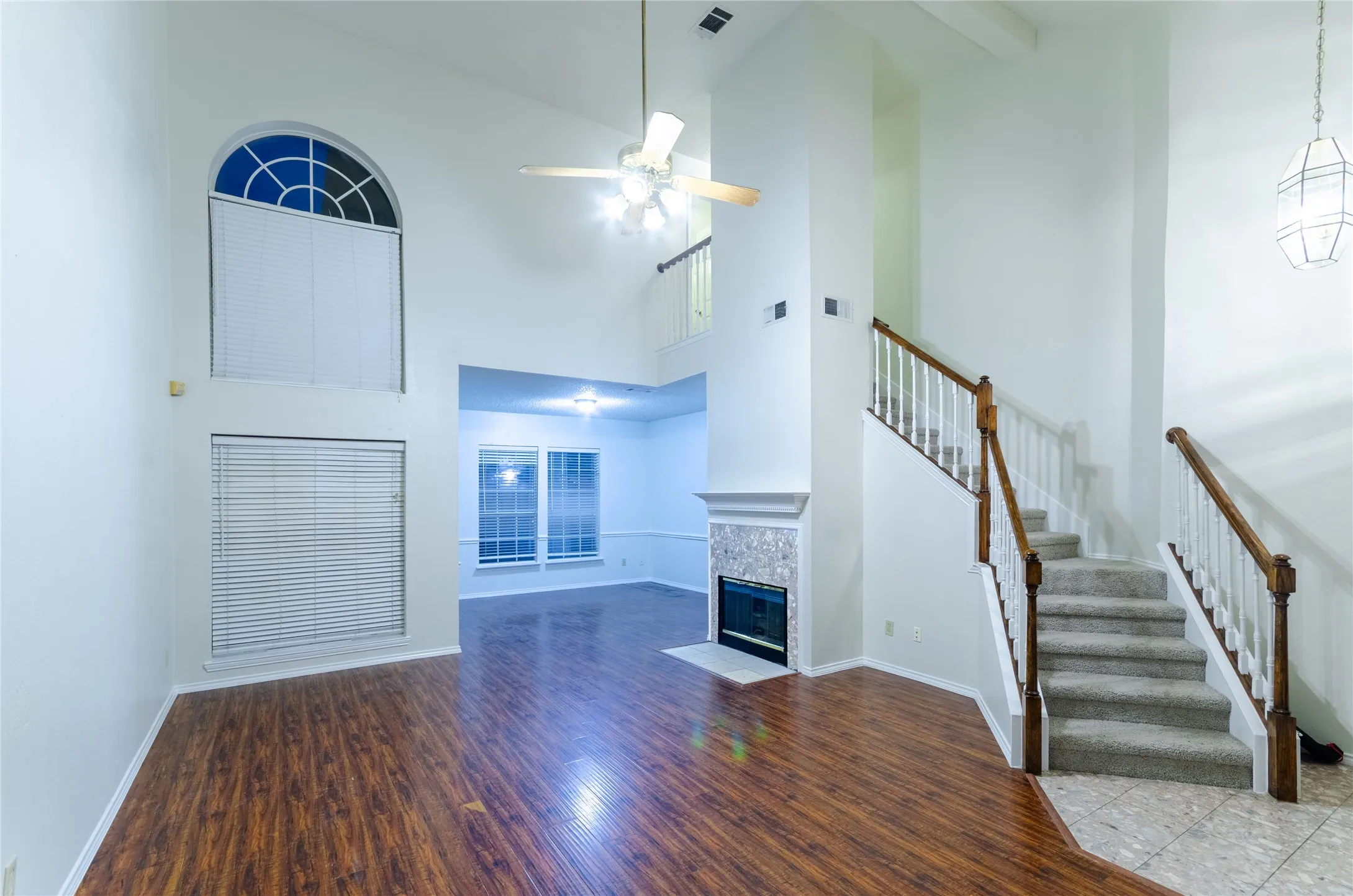 Vaulted ceilings, wood-finish flooring, staircase with wood handrails, fireplace with decorative tile surround, and an arched window