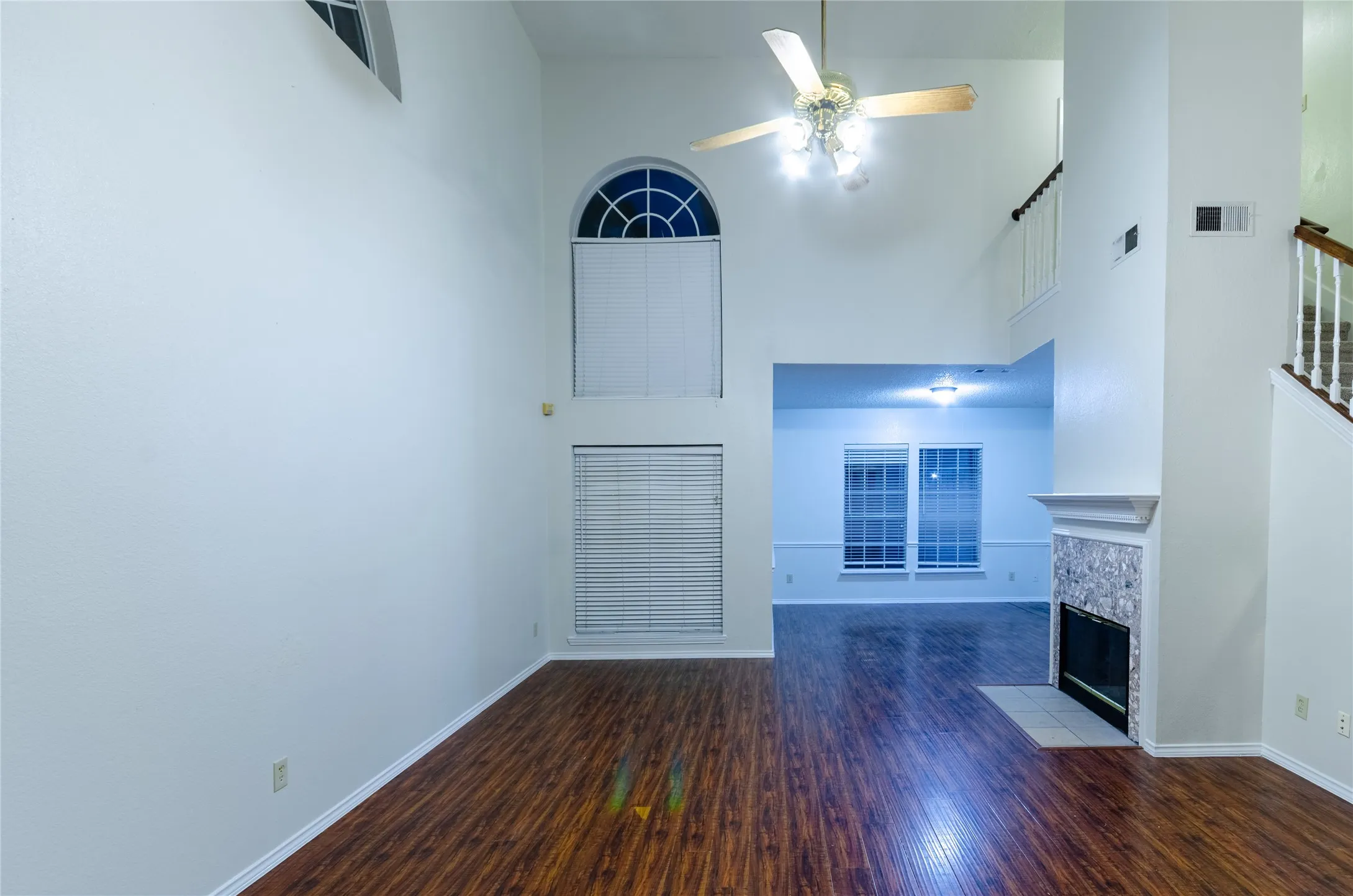 Vaulted ceiling with an arched window, wood-finish flooring, fireplace with a decorative tile surround, and a ceiling fan