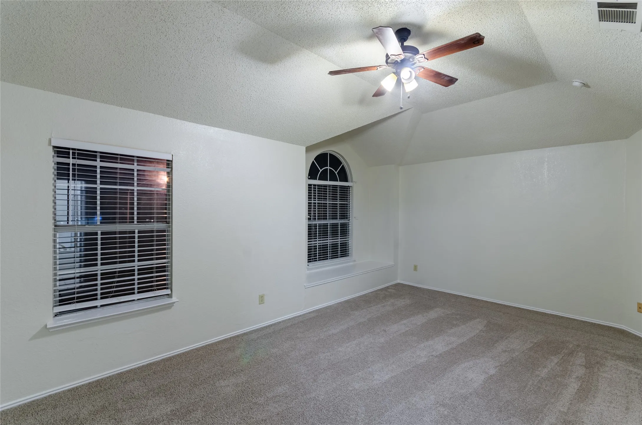 Primary Bedroom with Vaulted ceiling with a ceiling fan, arched window, rectangular window, and carpeted flooring