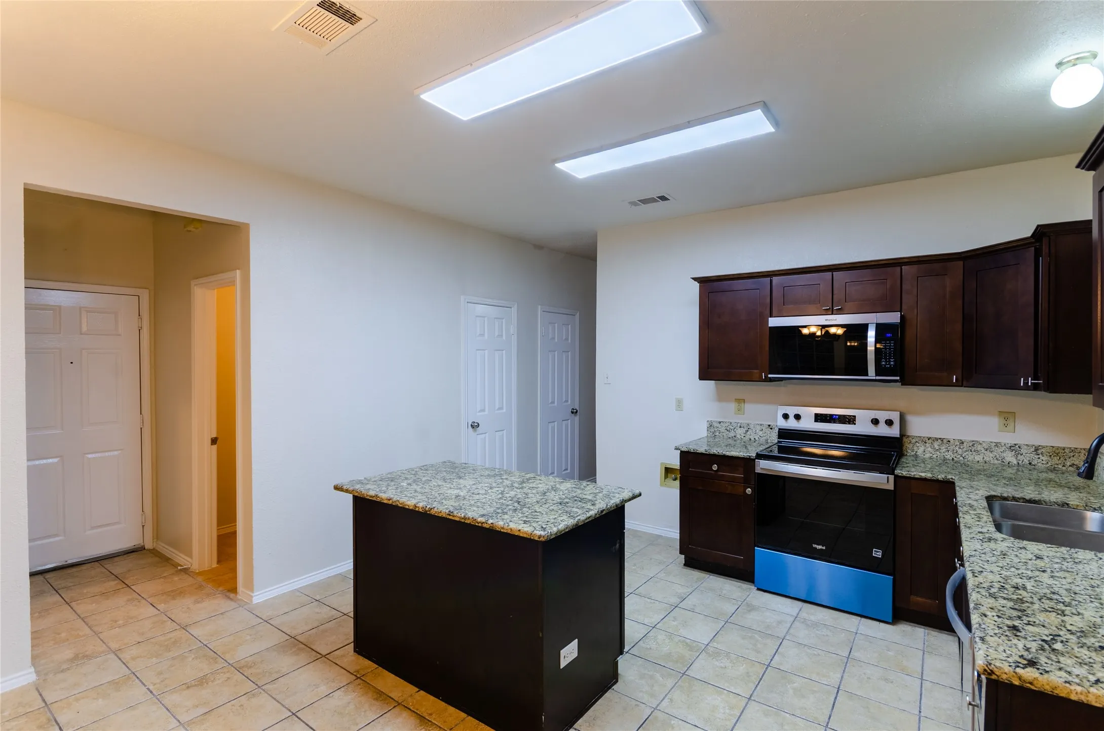 Kitchen featuring dark wood-finish cabinetry, granite countertops, a stainless steel electric range, an integrated microwave, and a central island with a granite surface