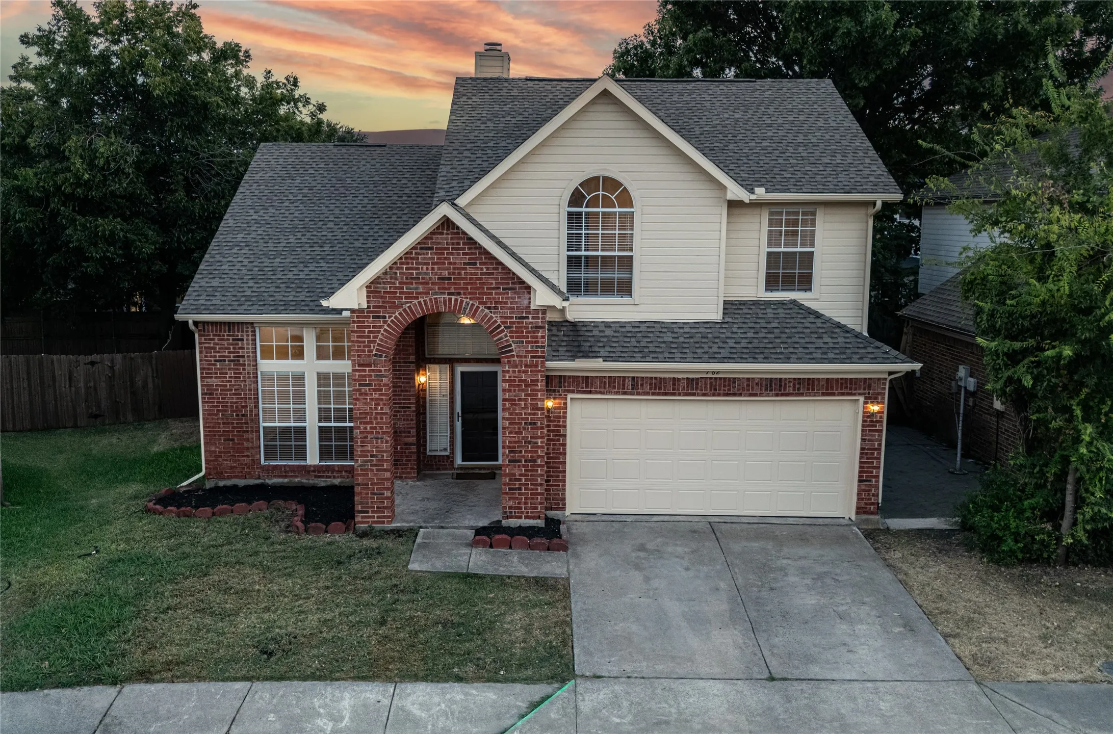 Brick and siding exterior with an arched entryway, attached two-car garage, and established landscaping