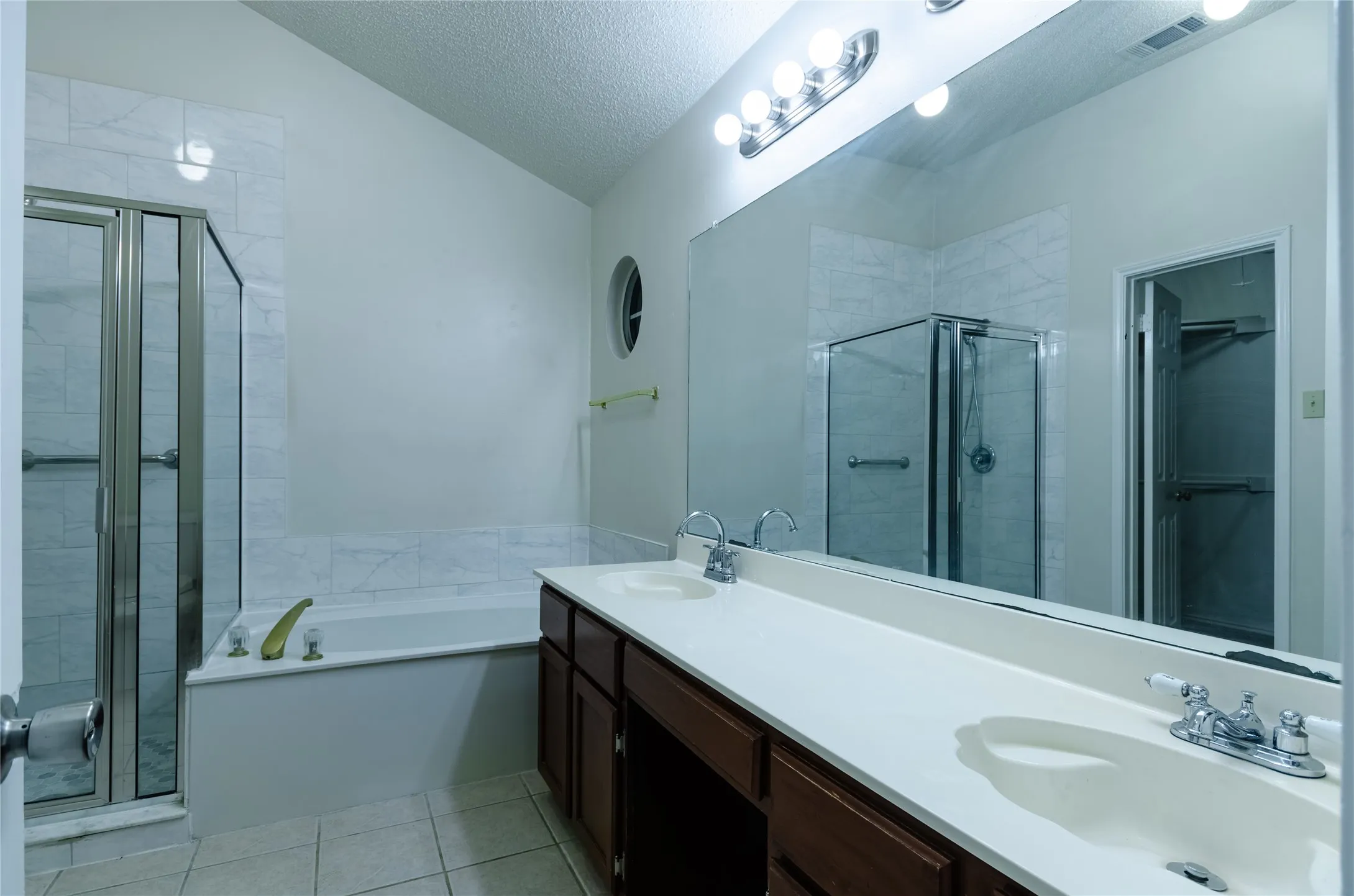 Dual vanity with integrated sinks, expansive wall-mounted mirror, enclosed shower with glass doors, built-in bathtub, and ceramic tile flooring