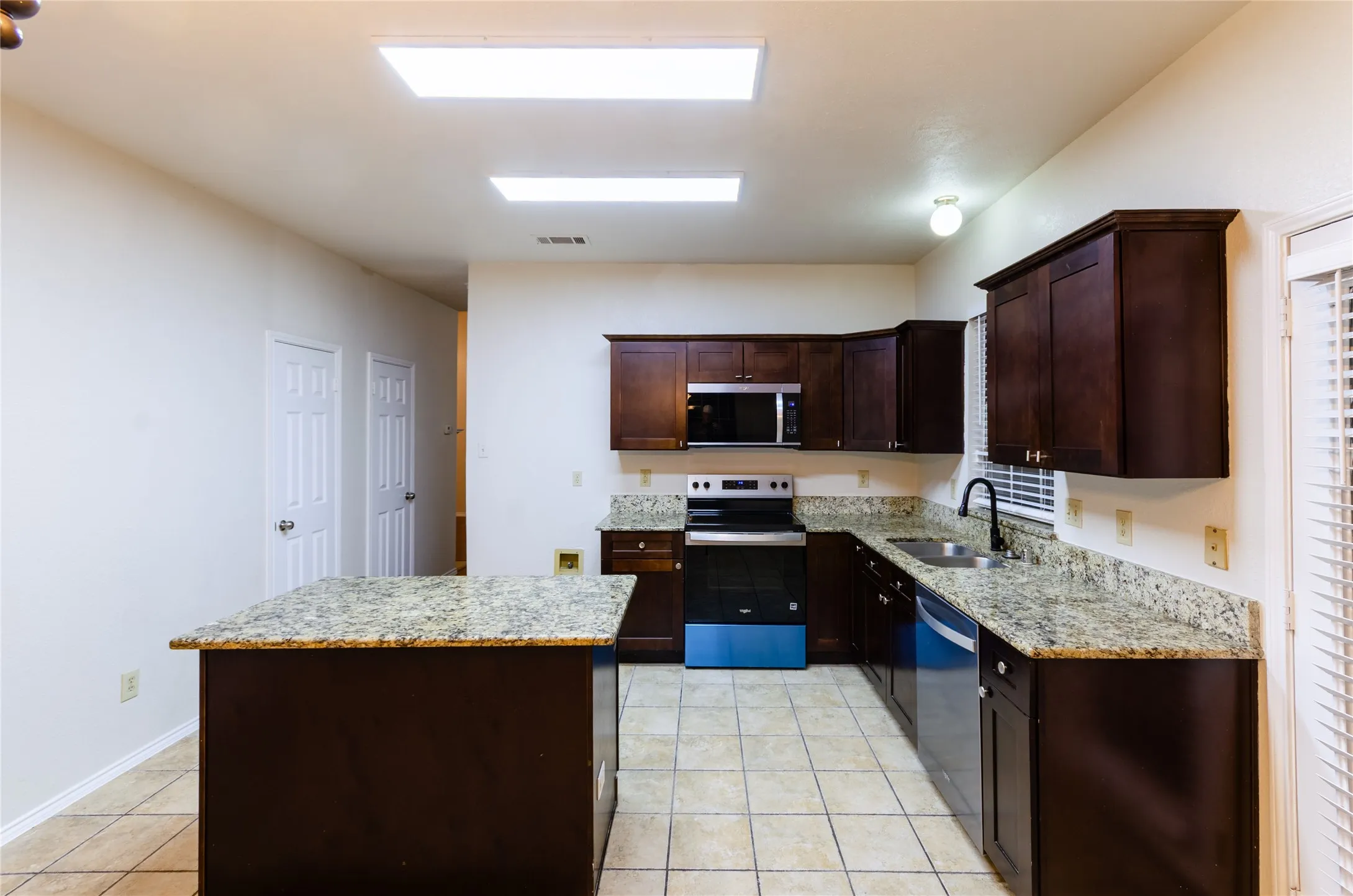 Kitchen featuring dark wood cabinetry, light-toned countertops, tile flooring, and stainless steel appliances