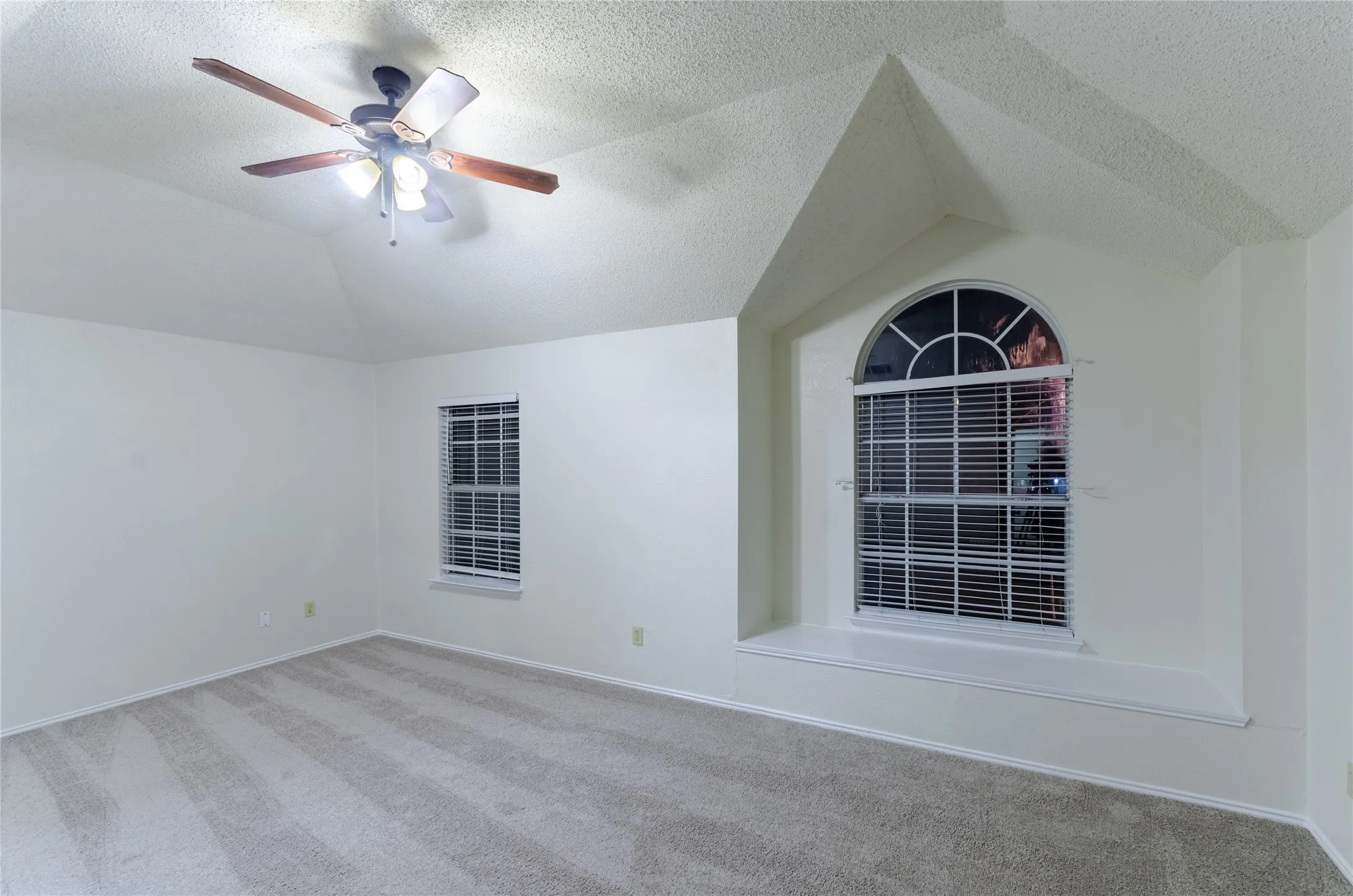 Primary Bedroom   featuring vaulted ceilings, a ceiling fan with integrated lighting, plush carpeting, and an architectural focal point with arched transom window and built-in shelving