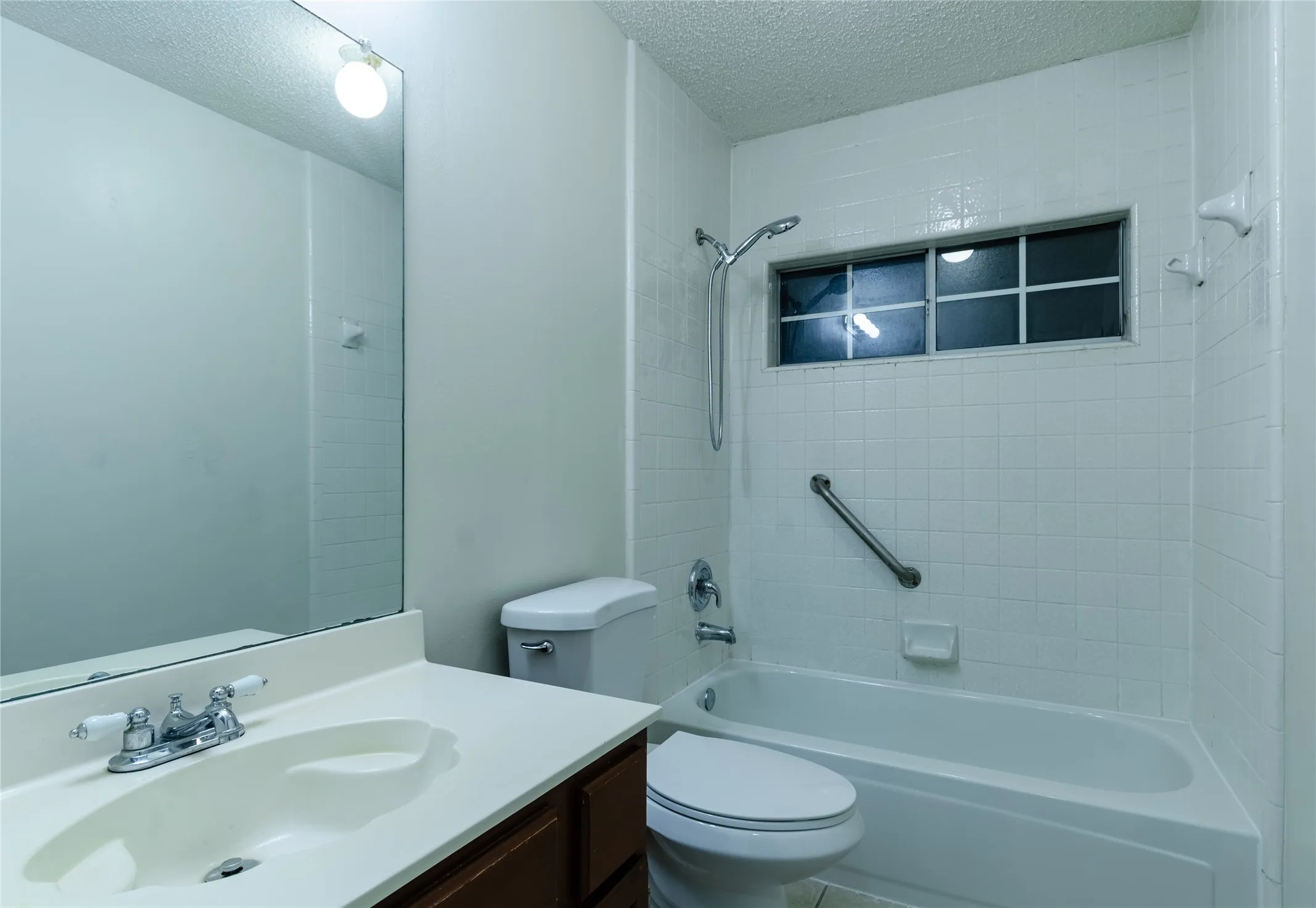 White tiled bath and shower combination with a grab bar and a window