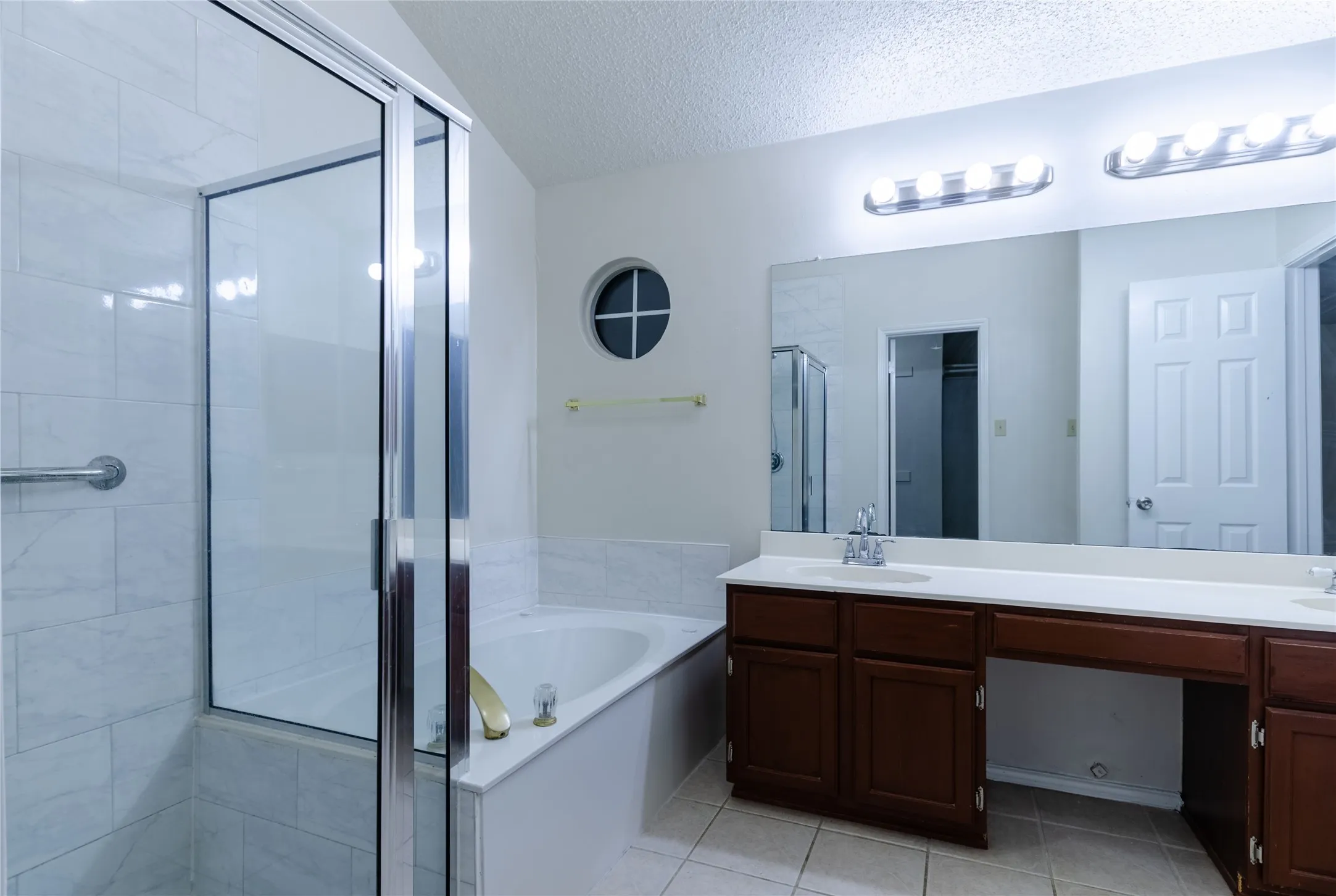 Walk-in shower with clear glass enclosure, corner soaking tub, dual vanity with wood cabinetry and expansive mirror, and tile flooring