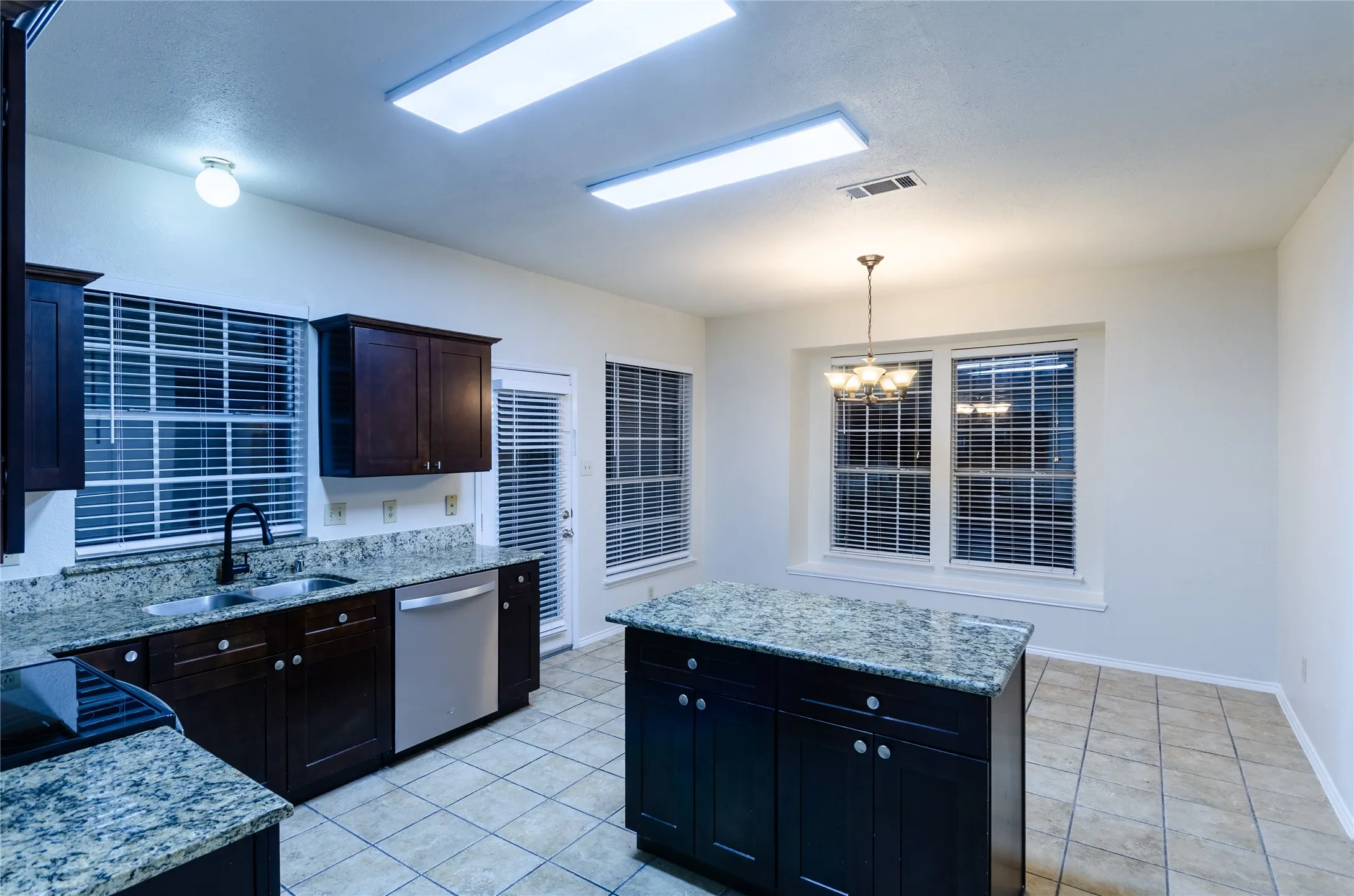 Kitchen featuring granite countertops, dark wood-finish cabinetry, stainless steel dishwasher, a center island, and tile flooring