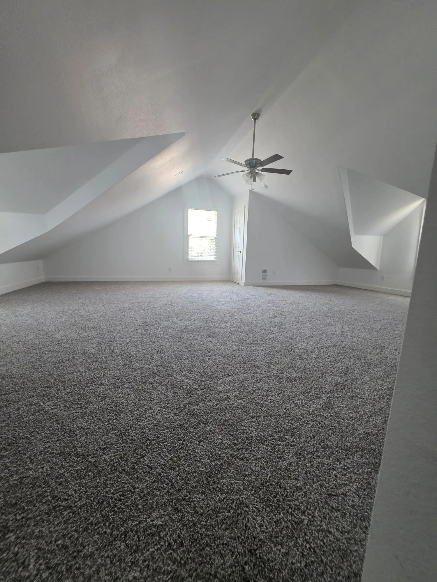 Carpeted room with sloped ceilings, a ceiling fan, and a window providing natural light