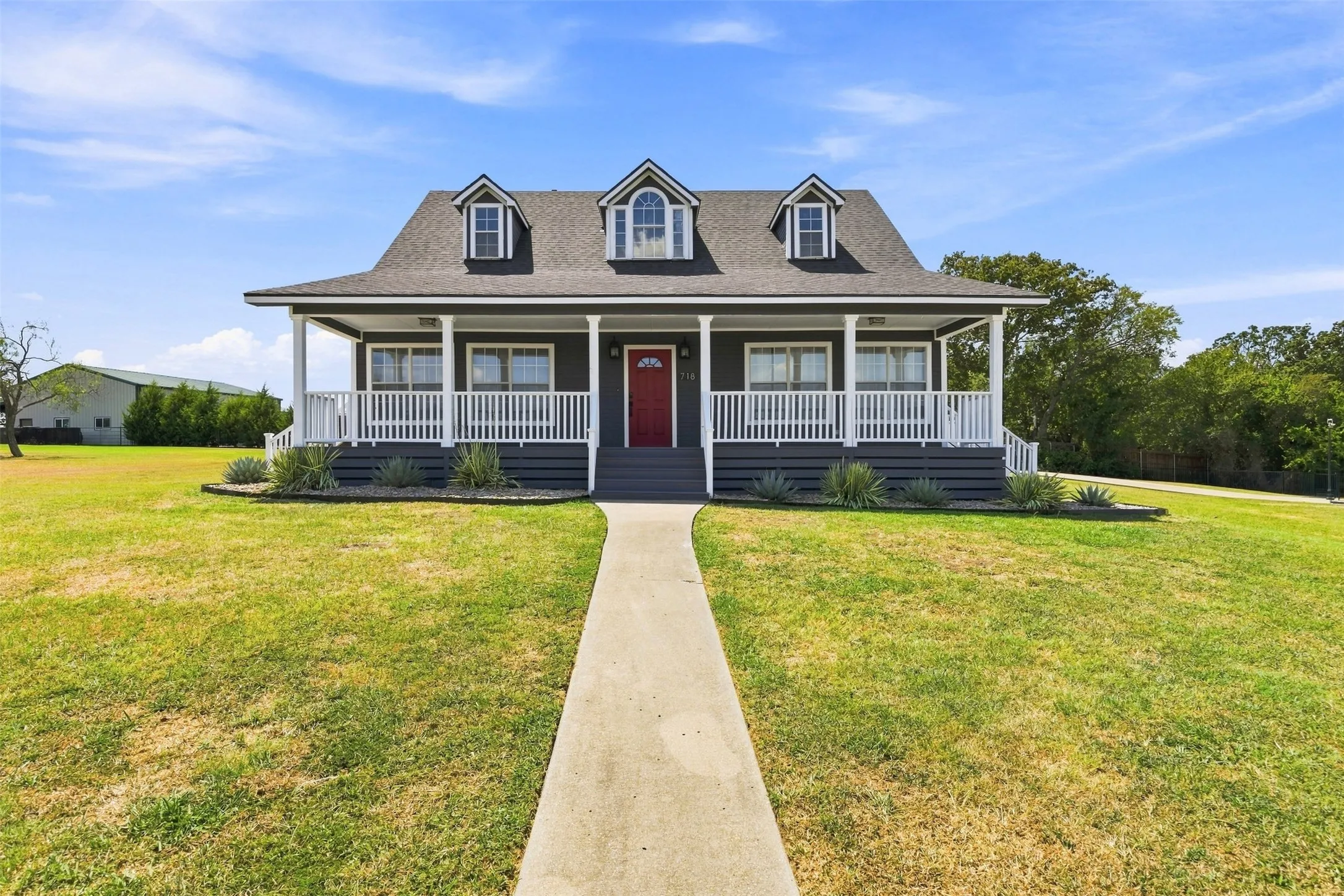 Classic dormer windows, covered front porch, white railing, vibrant red entry door, and manicured landscaping